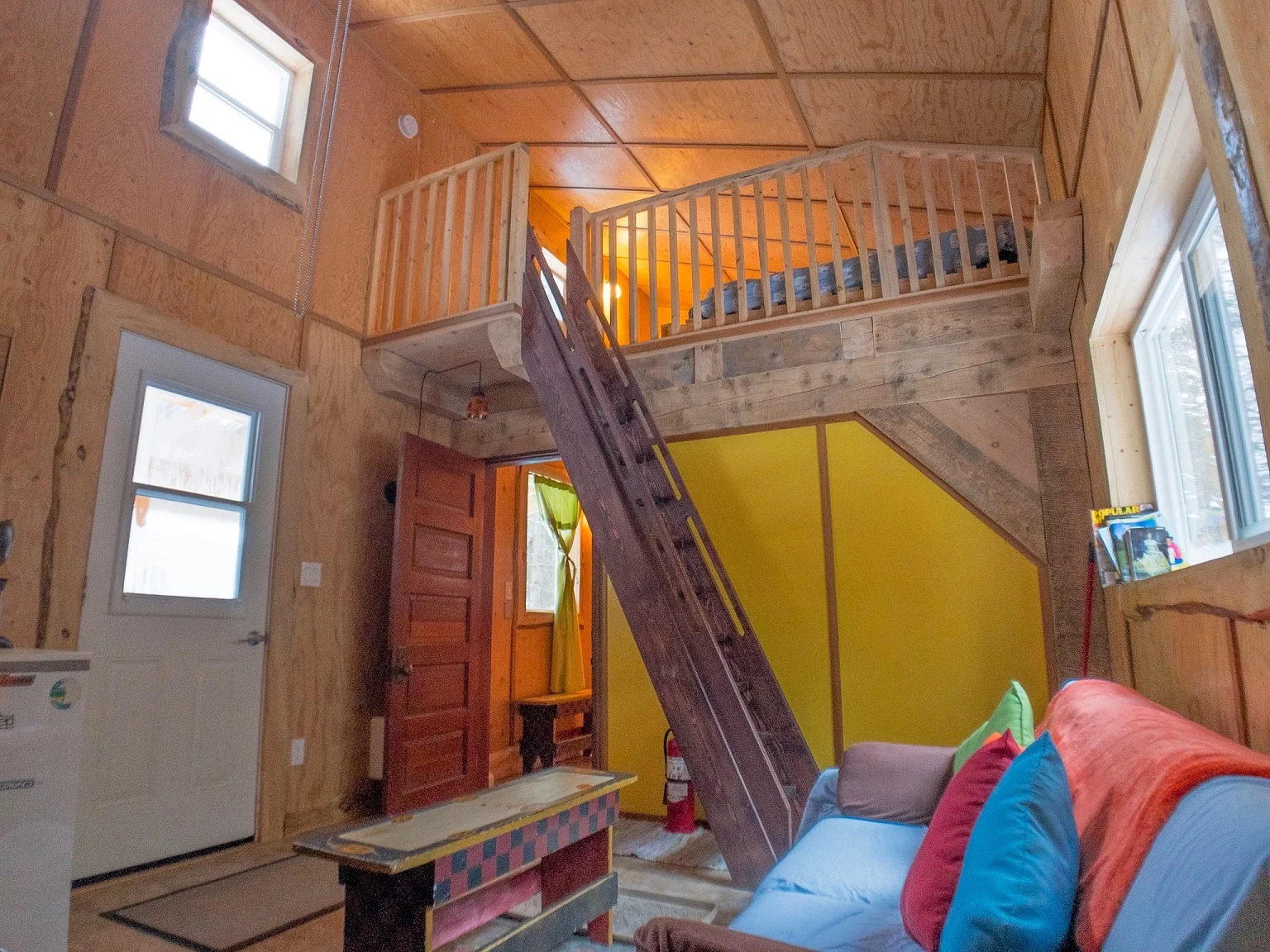 The MervInn This spacious cabin has two separate bedrooms, one on the main floor, and one in the upstairs loft. It also has a living room and a wide porch. It’s the perfect choice for a family or group of friends and nestled right in to the trees. Sleeps six with one double bed, two single beds in loft and a pull out sofa. Linens, power and VIP access included.