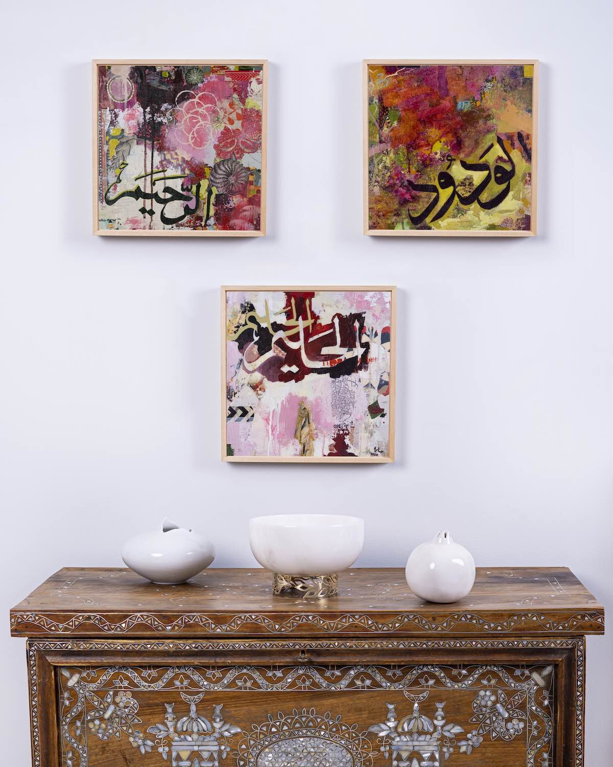 Compassion, Love in Rose and Forbearance framed together on a wall above a carved wooden console table with white ceramic vessels, from the Hu Collection by Sara Kabariti