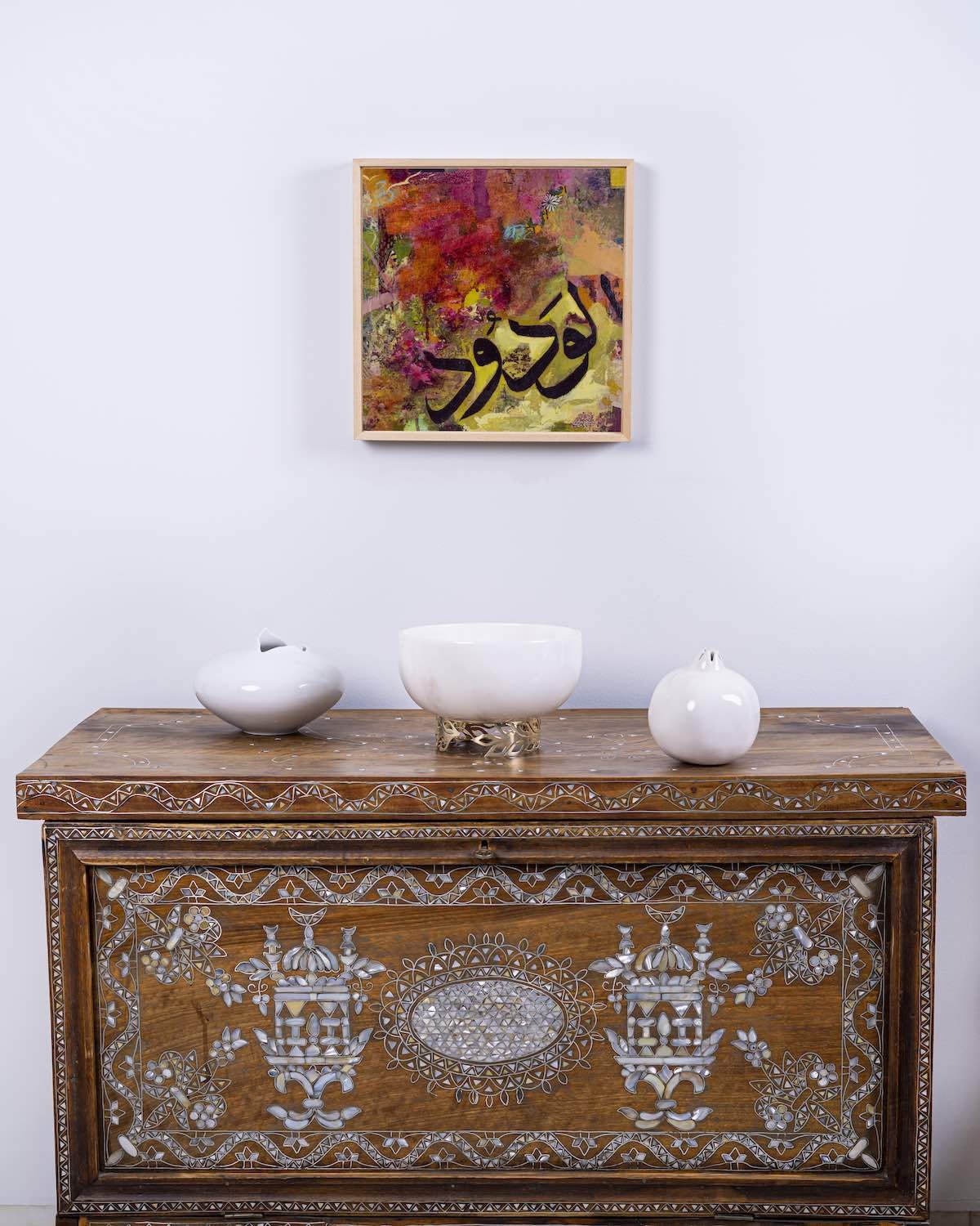 Love in Rose, framed mixed media painting depicting the Name Al-Wadud, from the Hu Collection, hung above a carved wooden console table with white ceramic vessels, 2020, by Sara Kabariti