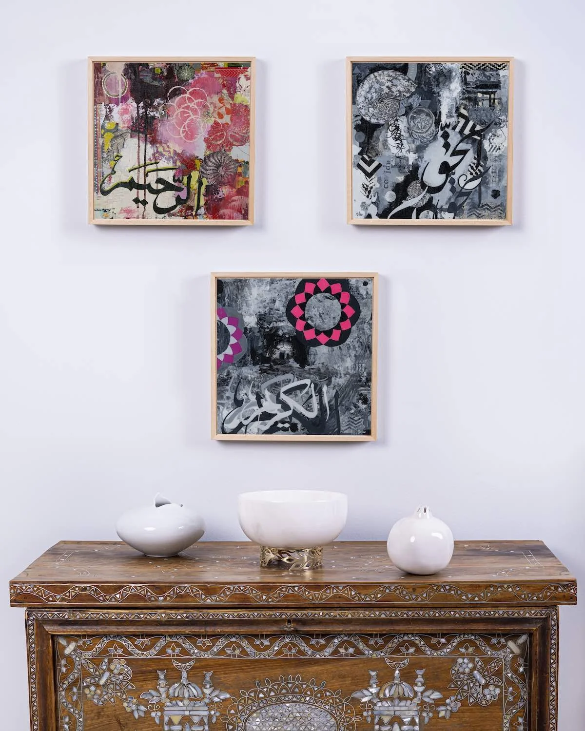 Compassion and Reality partially visible, with The Cave shown in full, framed together from the Hu Collection above a carved wooden console table with white ceramic vessels, mixed media on panel by Sara Kabariti
