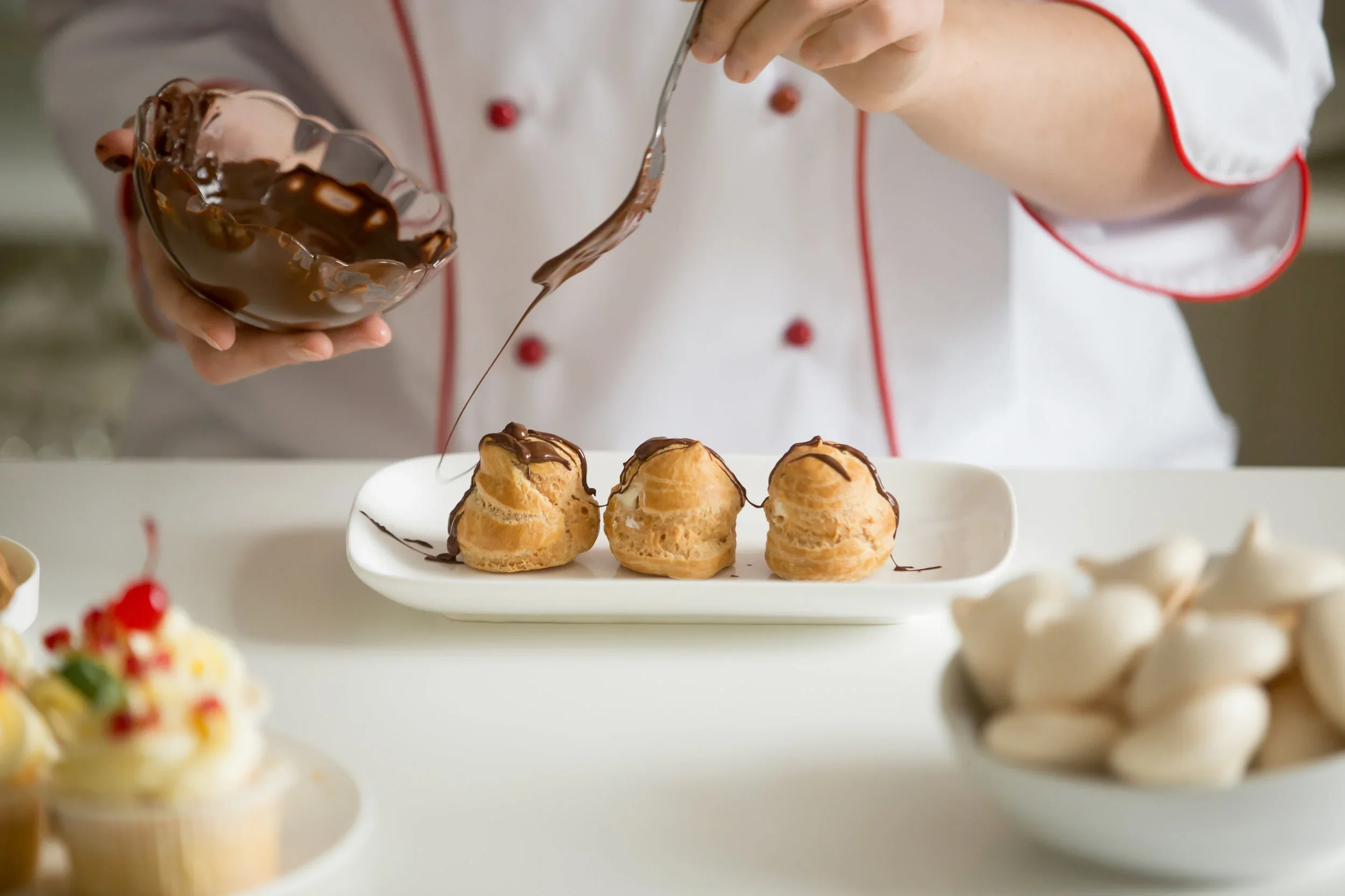 Pastry chef drizzling chocolate over cream puffs.webp