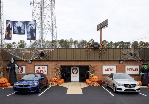 Halloween-decorated auto repair shop with pumpkins, spider webs, and spooky figures, featuring BMW and Mercedes-Benz vehicles
