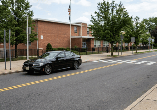 Black BMW sedan parked near a school crosswalk on a quiet neighborhood street
