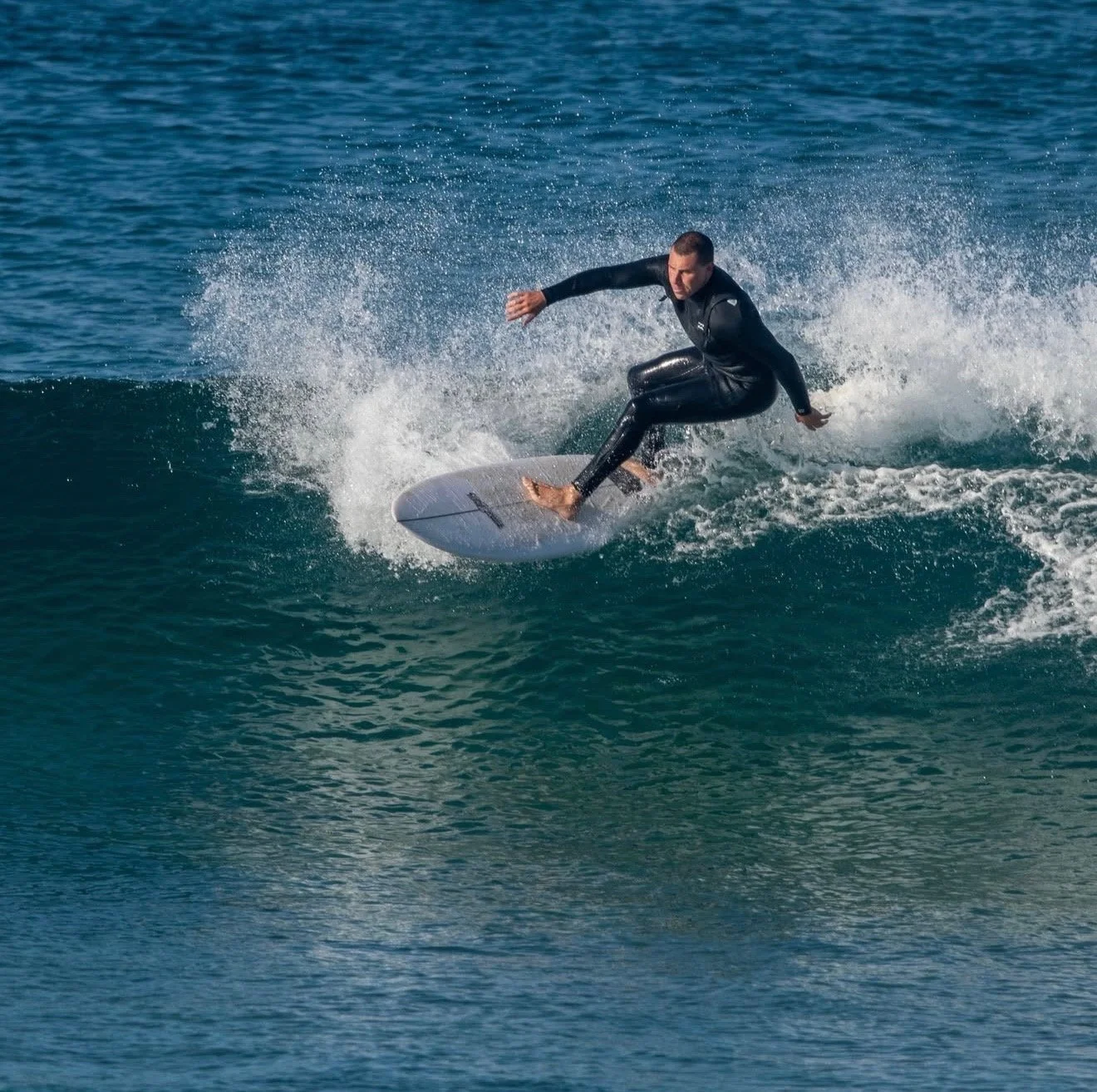 A man wearing a black wetsuit surfing on a wave in the ocean.