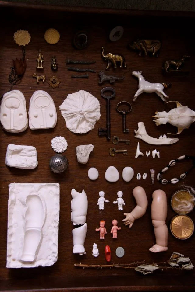 Collection of various small objects including animal figures, keys, small figurines, shells, and miscellaneous items spread on a wooden surface. Community artist working with MIND charity, wellbeing, mental health