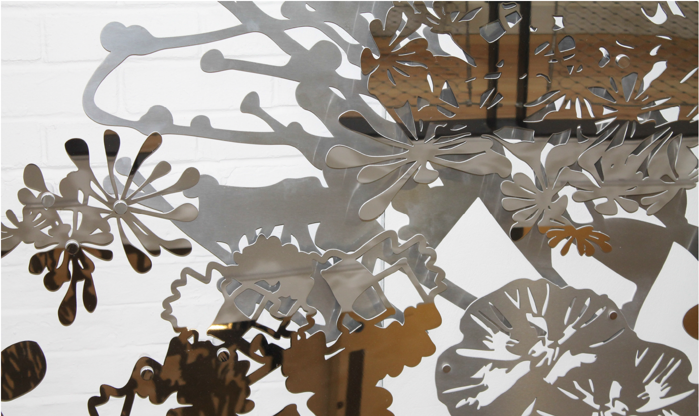 Close-up of a decorative metal sculpture with floral and circular patterns, reflected on a mirror surface.