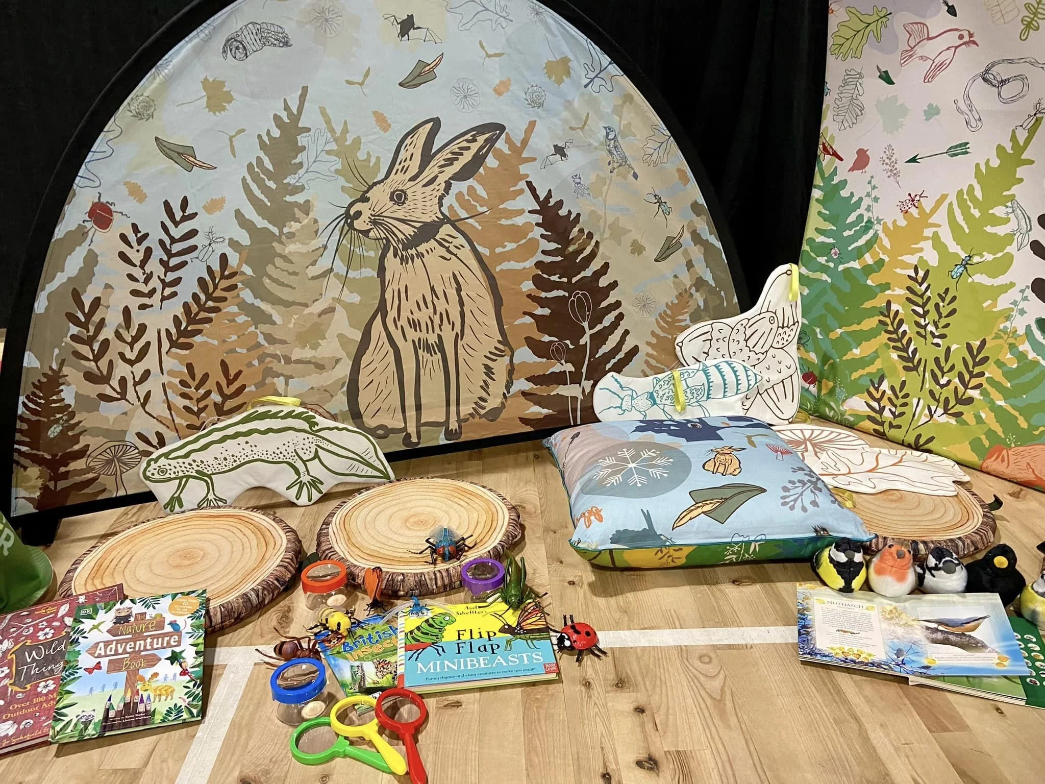 A nature-inspired display with a woodland backdrop featuring animals like a deer and insects, along with children's books, wooden log slices, and small animal-themed toys and decor.