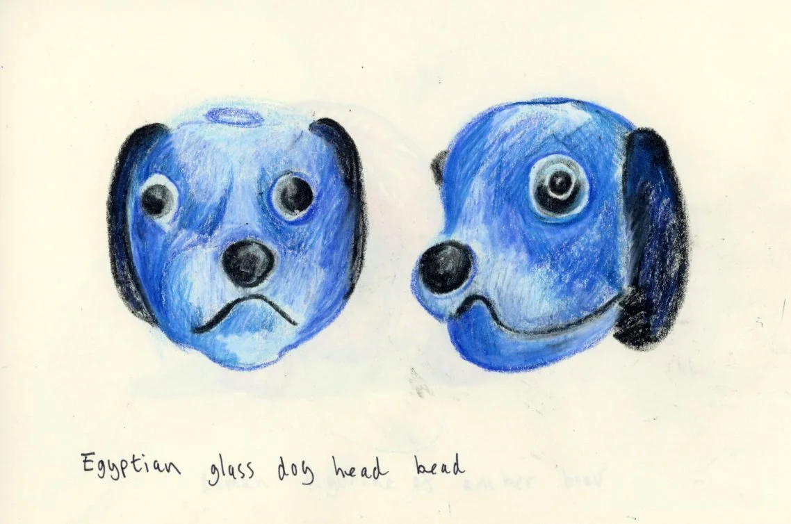 Drawing of a blue dog head with a sad face on the left and a happy face on the right, labeled 'Egyptian glass dog head bead'.