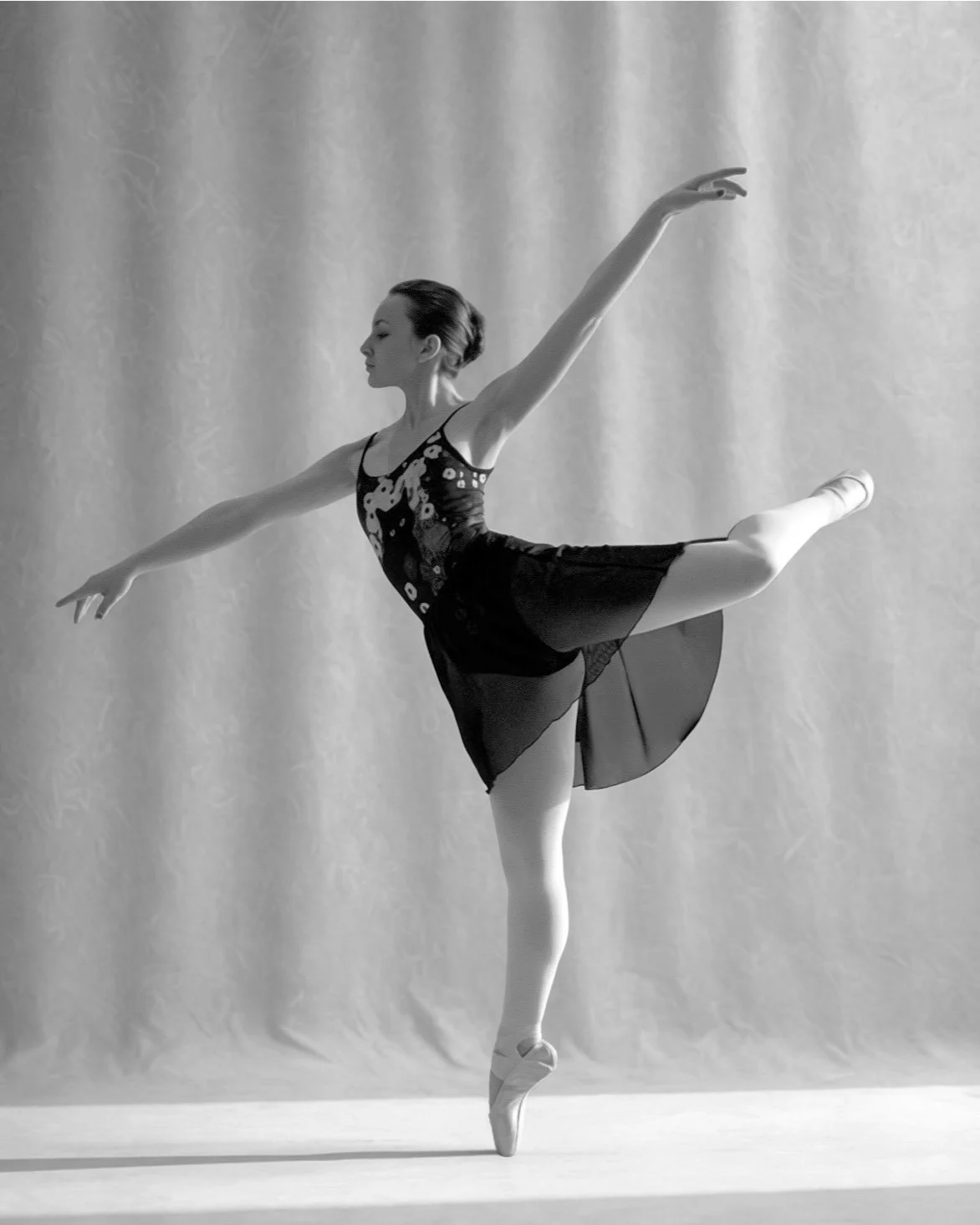 A ballet dancer in a black dress performing an arabesque pose on stage.