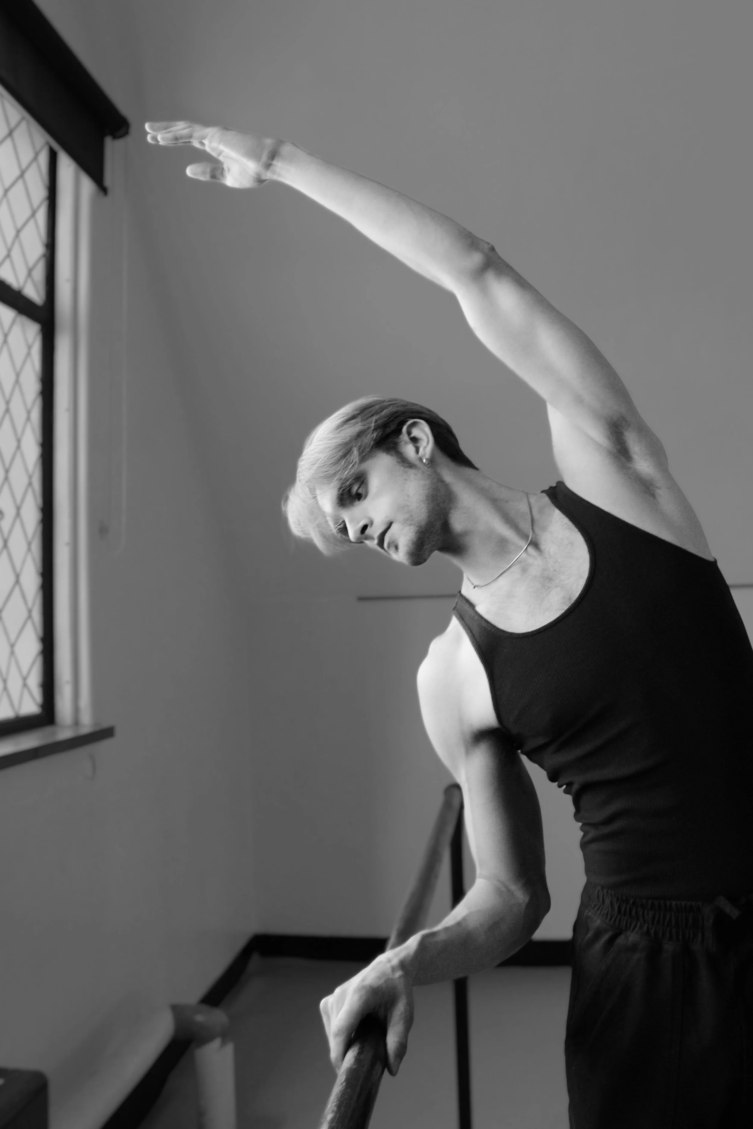 A young person stretching their arm over a ballet barre in a dance studio.