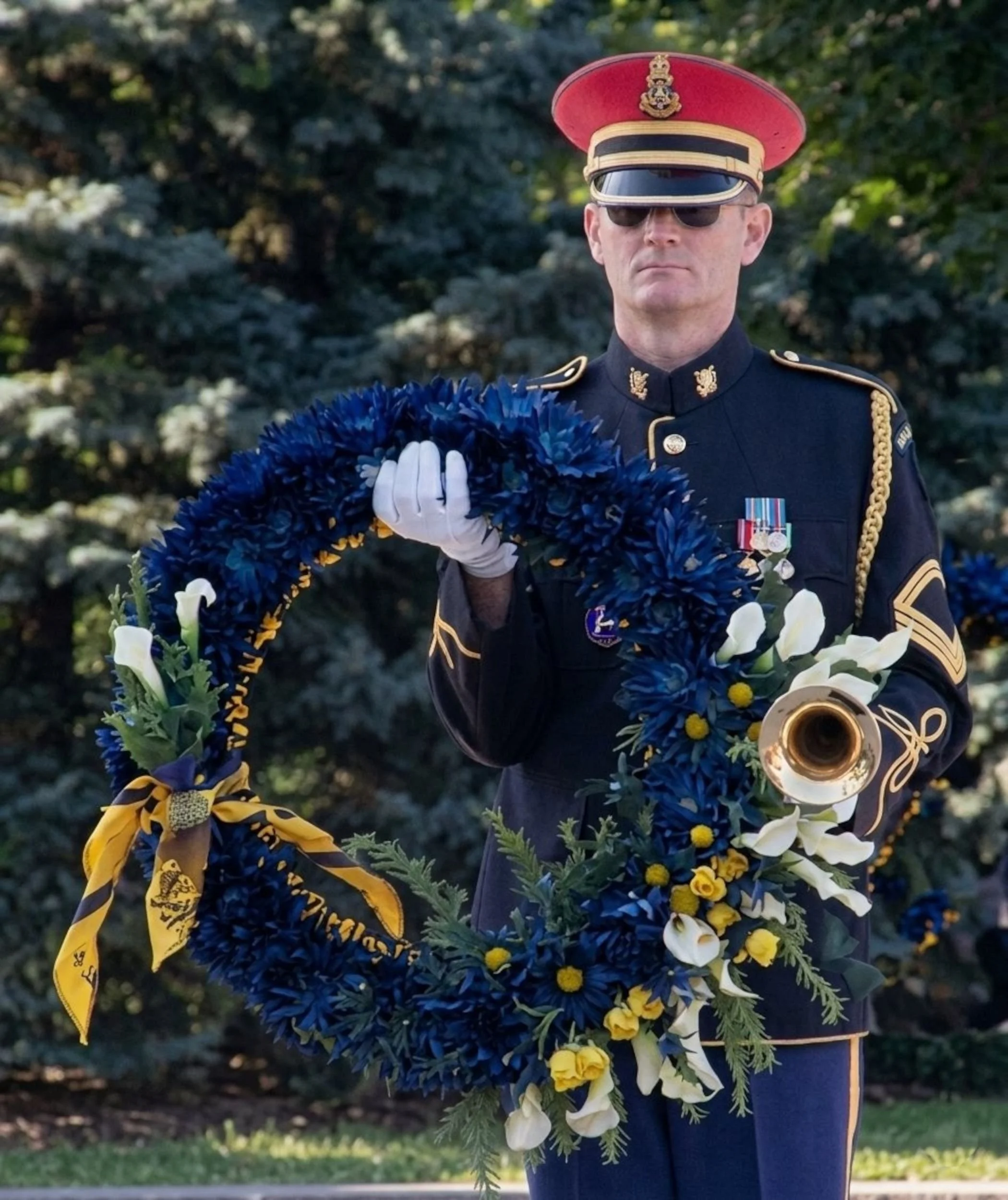A bugler holding a wreath in one hand, while his bugle is tucked underneath his other arm