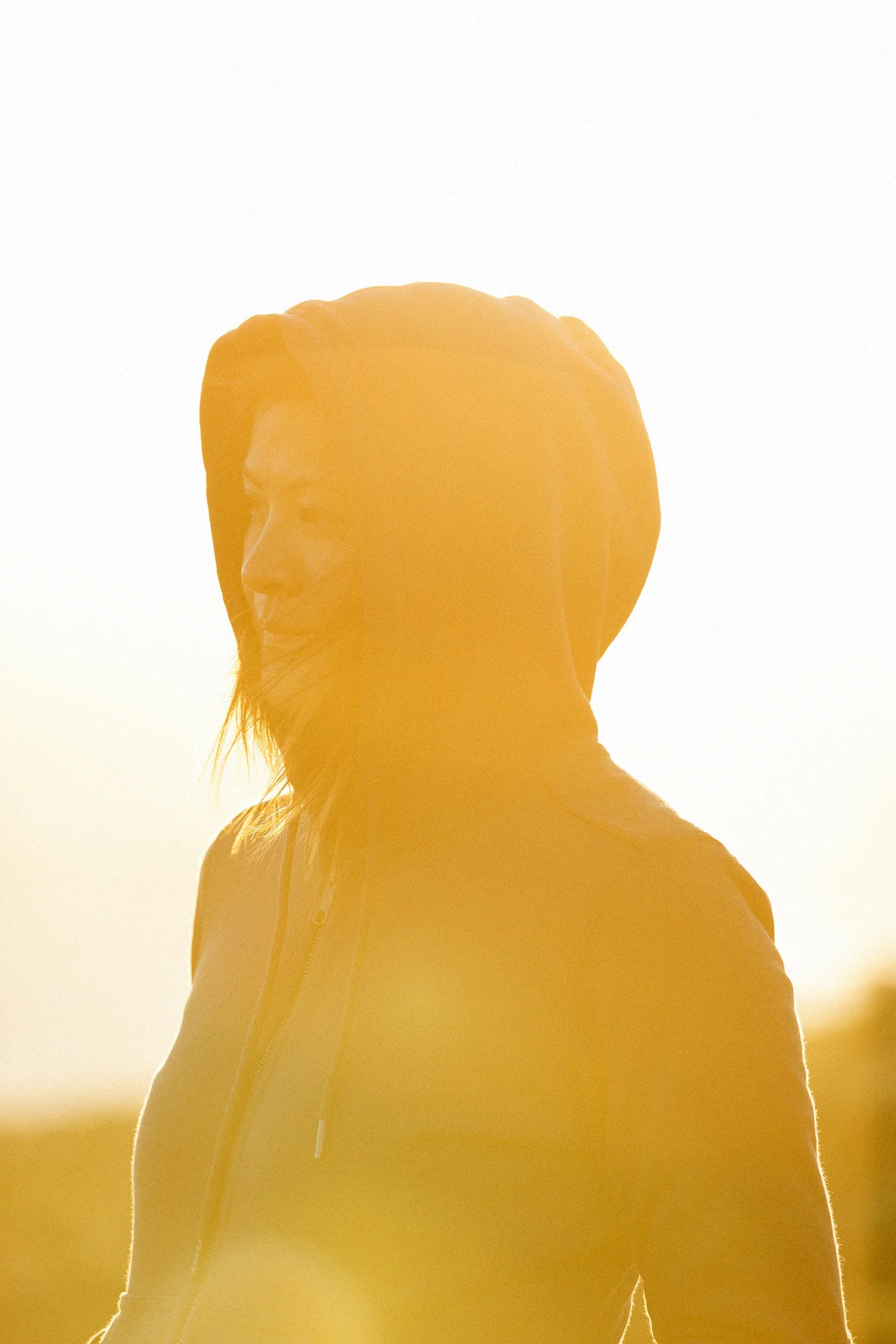 Golden hour lifestyle shot: Side profile of a smiling woman in a hoodie, captured at sunset for a commercial feel.