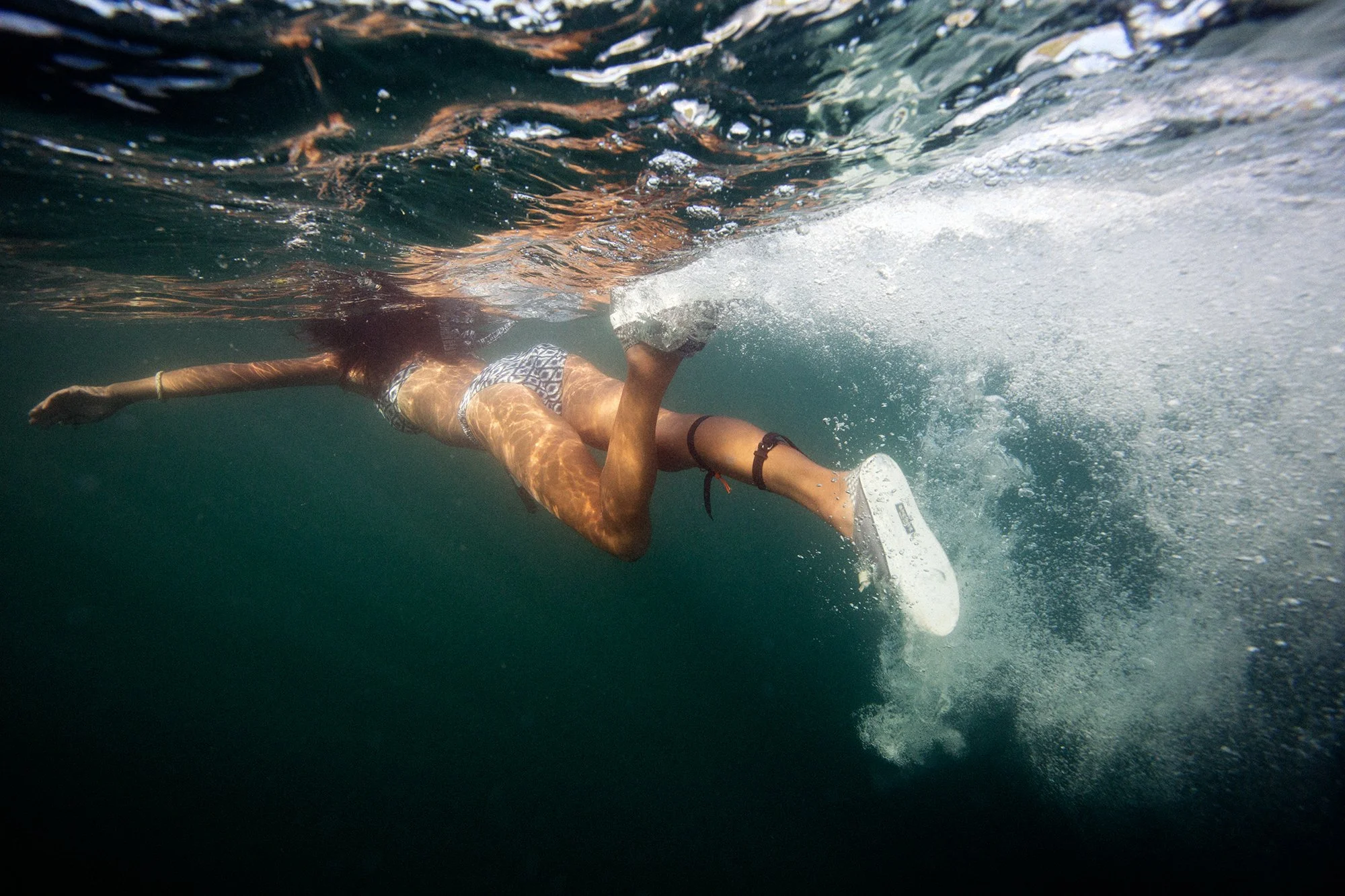 Person swimming underwater, wearing swimsuit, with a flipper on one foot, surrounded by bubbles.
