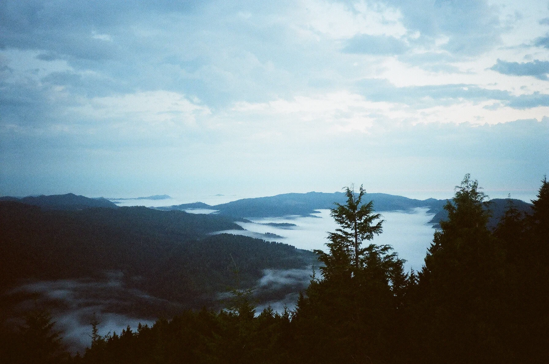 A scenic view of foggy mountain ranges with forested peaks and cloudy sky.