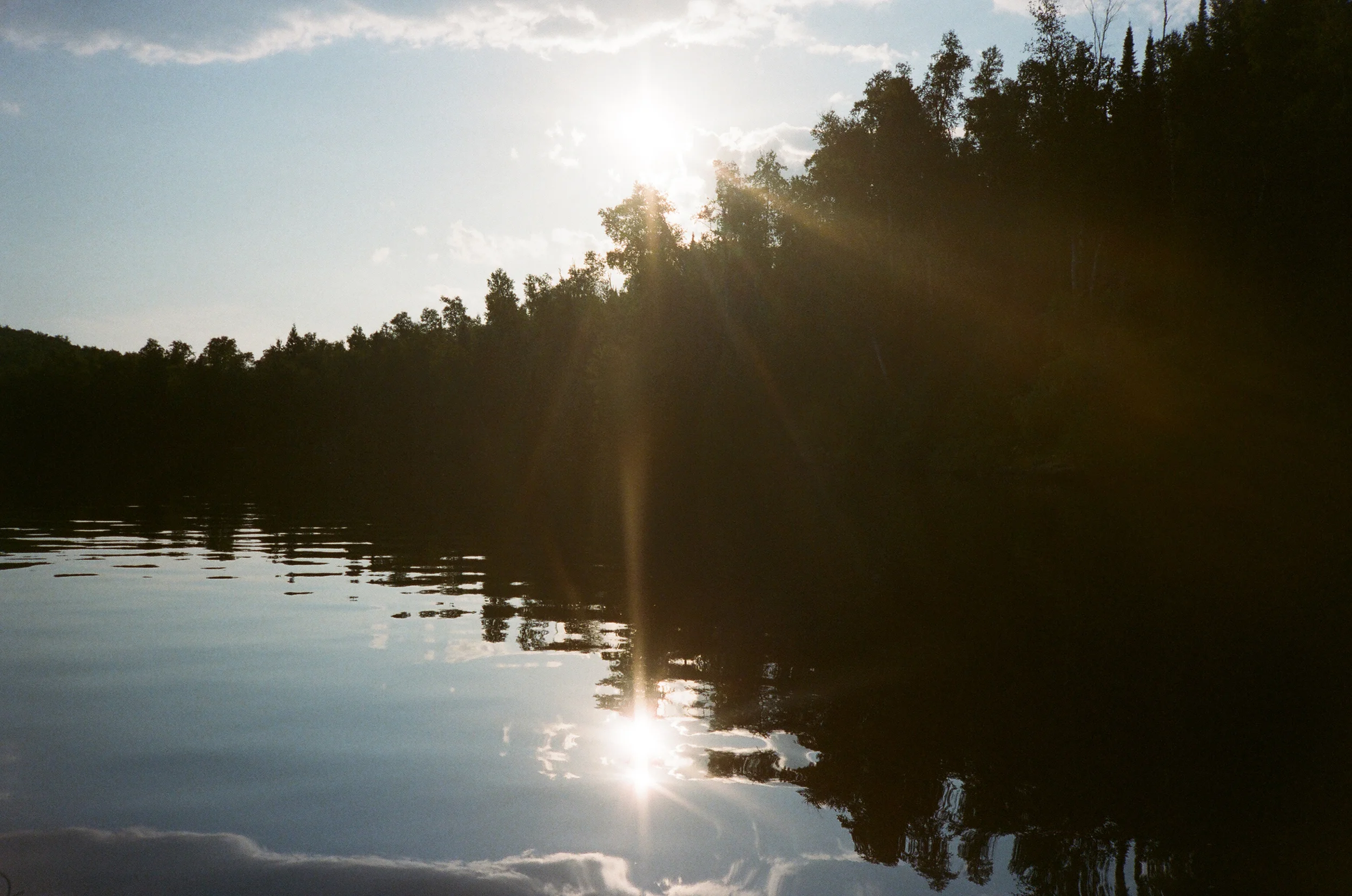 Sunset over a calm river with trees along the shoreline, reflected in the water.