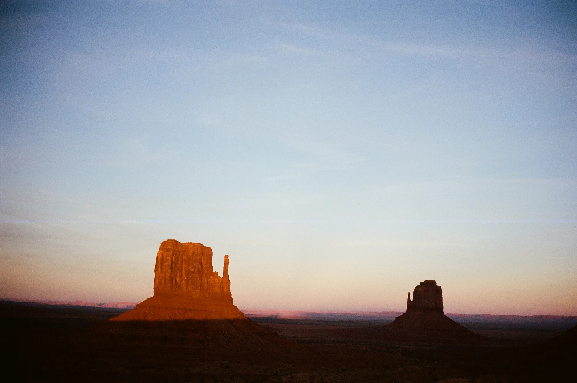 Two large rock formations in a desert landscape during sunset.