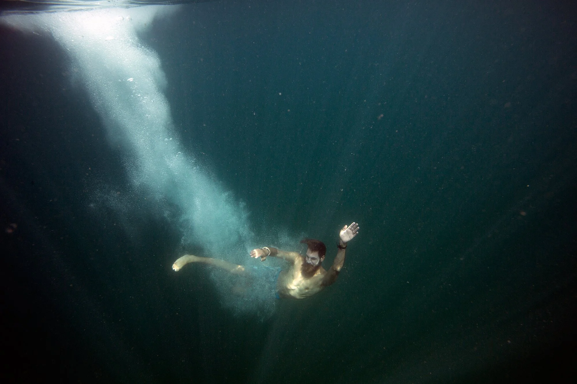 A man swimming underwater, wearing a wristwatch and white gloves, with bubbles trailing behind him.