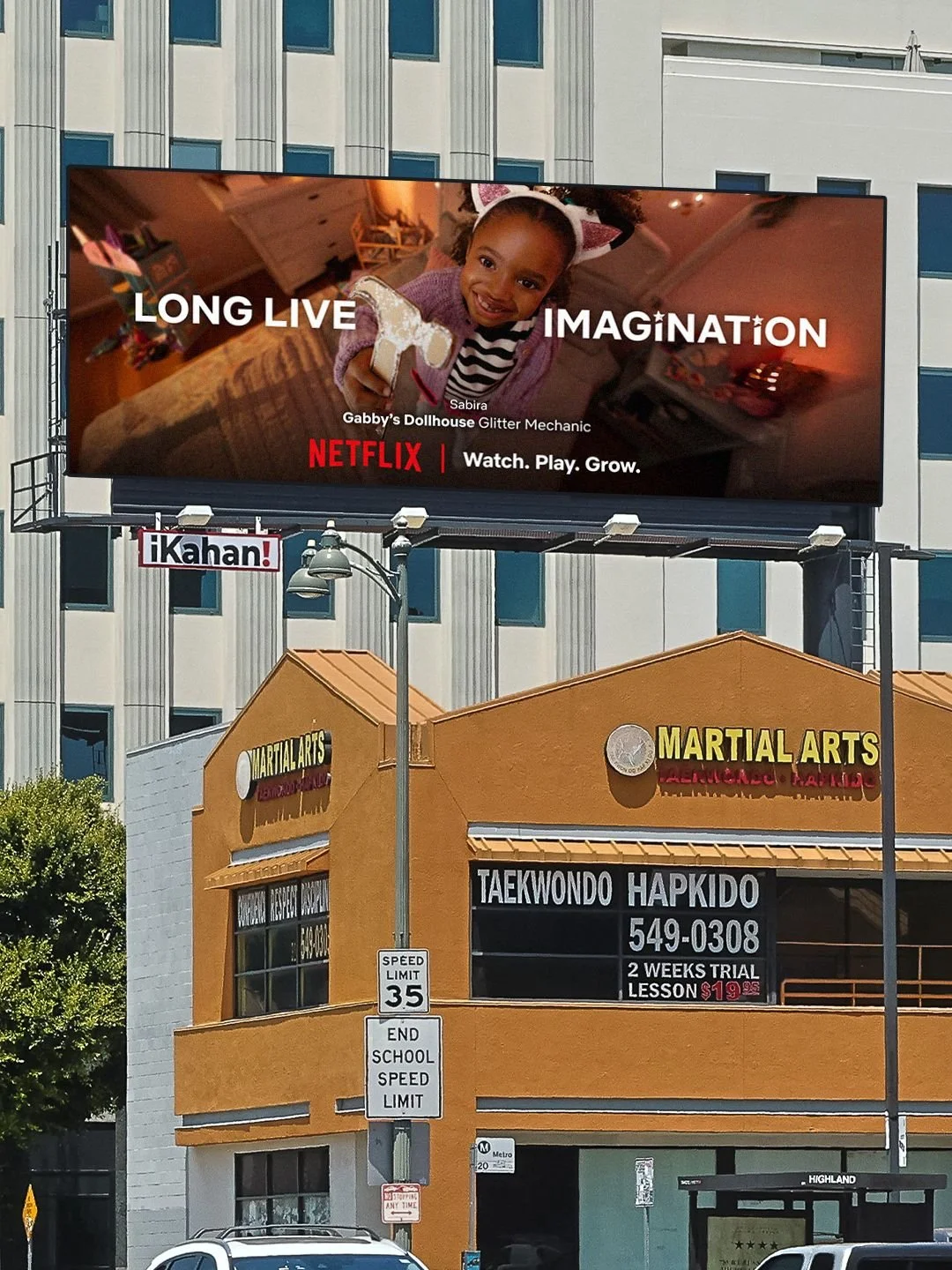 A large billboard advertisement for Netflix featuring a young girl holding a glittery unicorn toy, with helicopter ears and a striped shirt, smiling. The background of the ad is warm-toned. Below, there is a storefront for a martial arts school, with