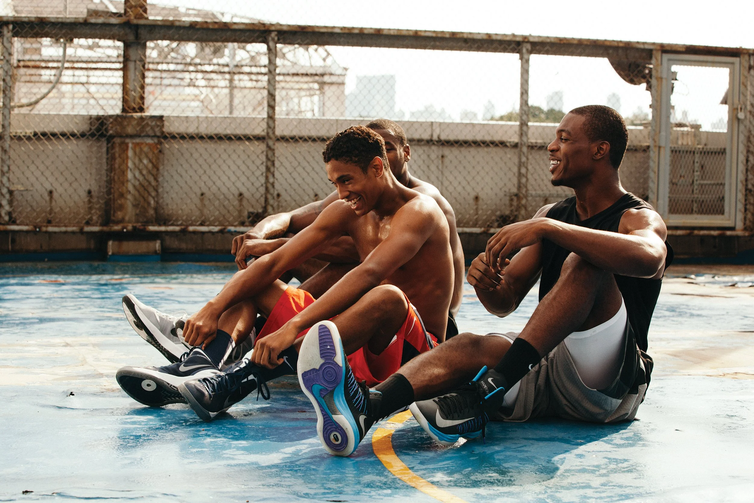 Four young men sitting on a basketball court, smiling and laughing.