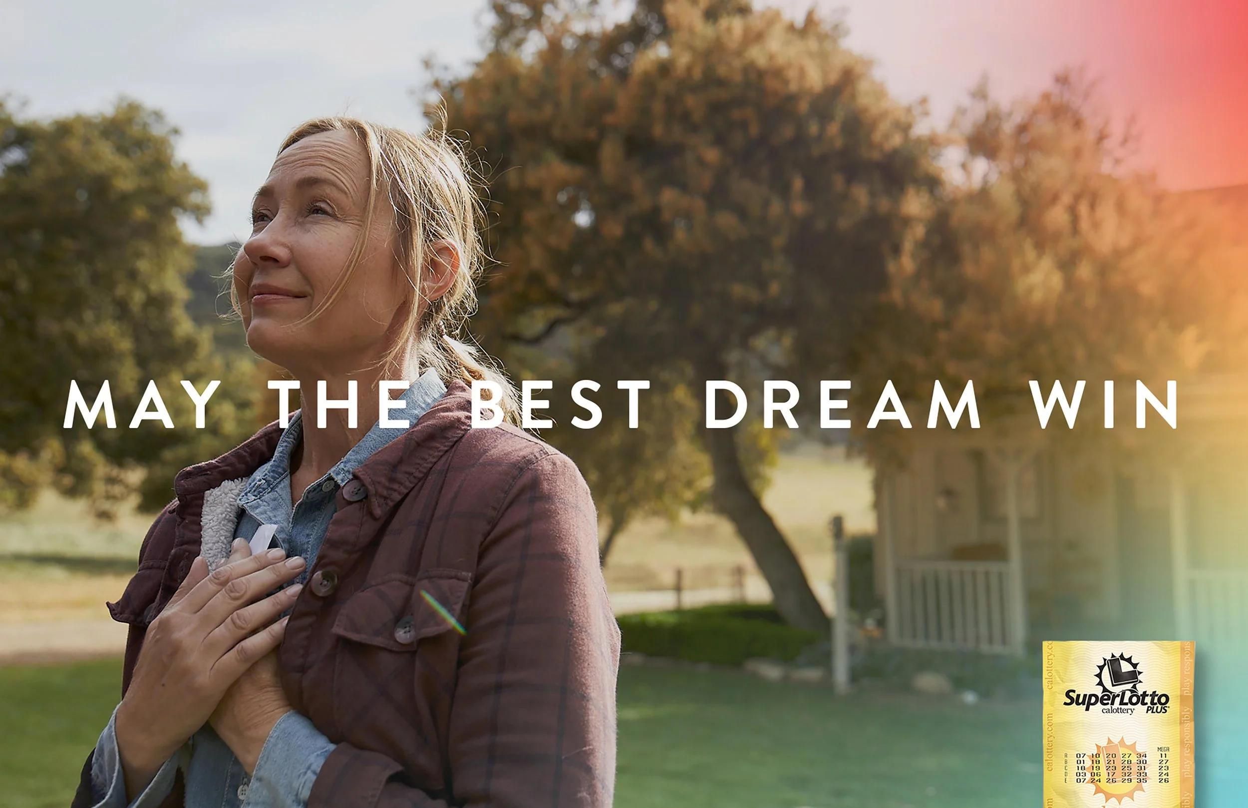 A woman outdoors during daytime, with one hand on her chest, smiling softly and looking ahead. Sunlit trees and a house are in the background. Text on image: "May the best dream win." A SuperLotto Plus ticket is in the lower right corner.