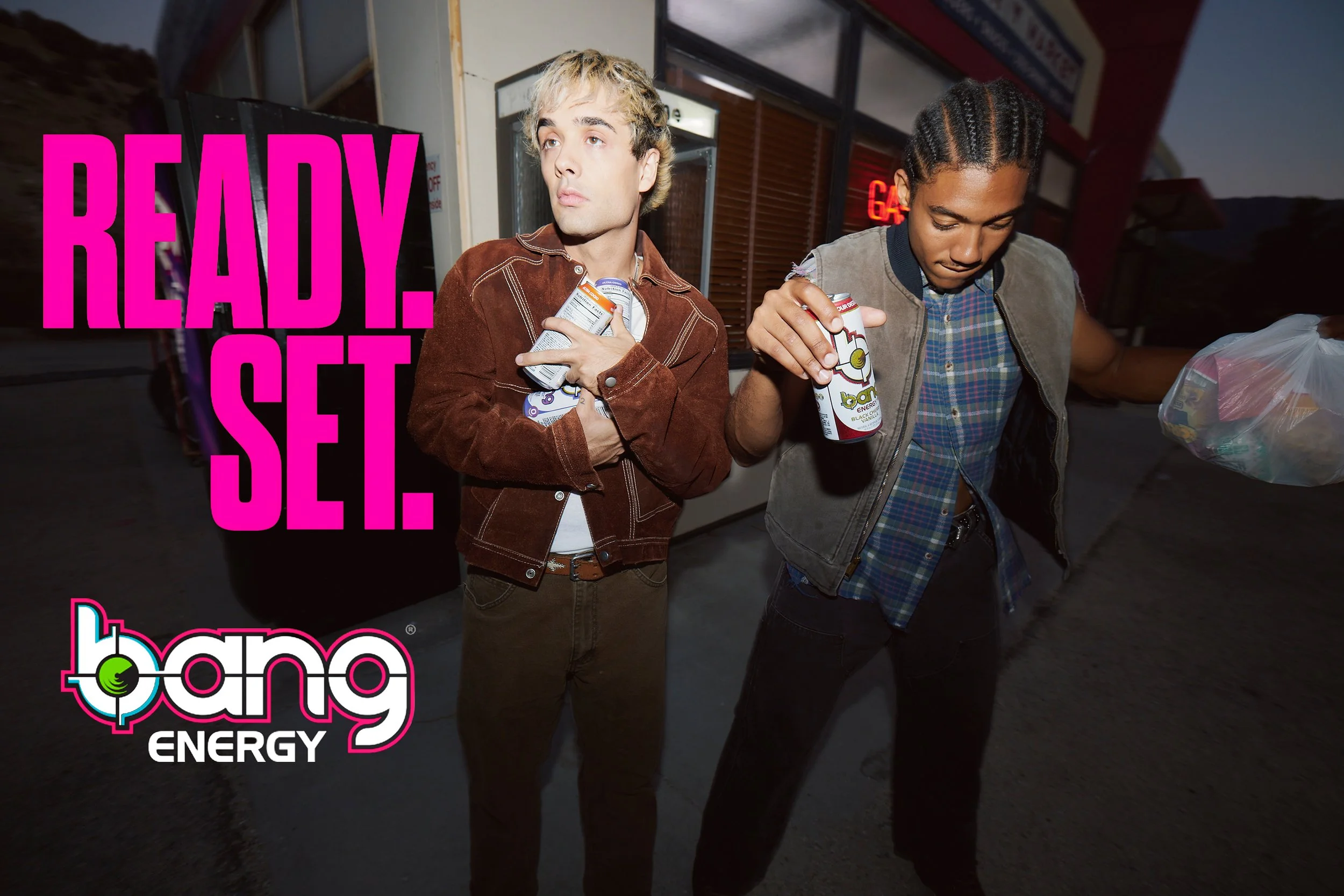 Two young men holding Bang energy drinks standing outside a store, with a large pink text overlay reading 'READY. SET.' and the Bang Energy logo in the bottom left corner.