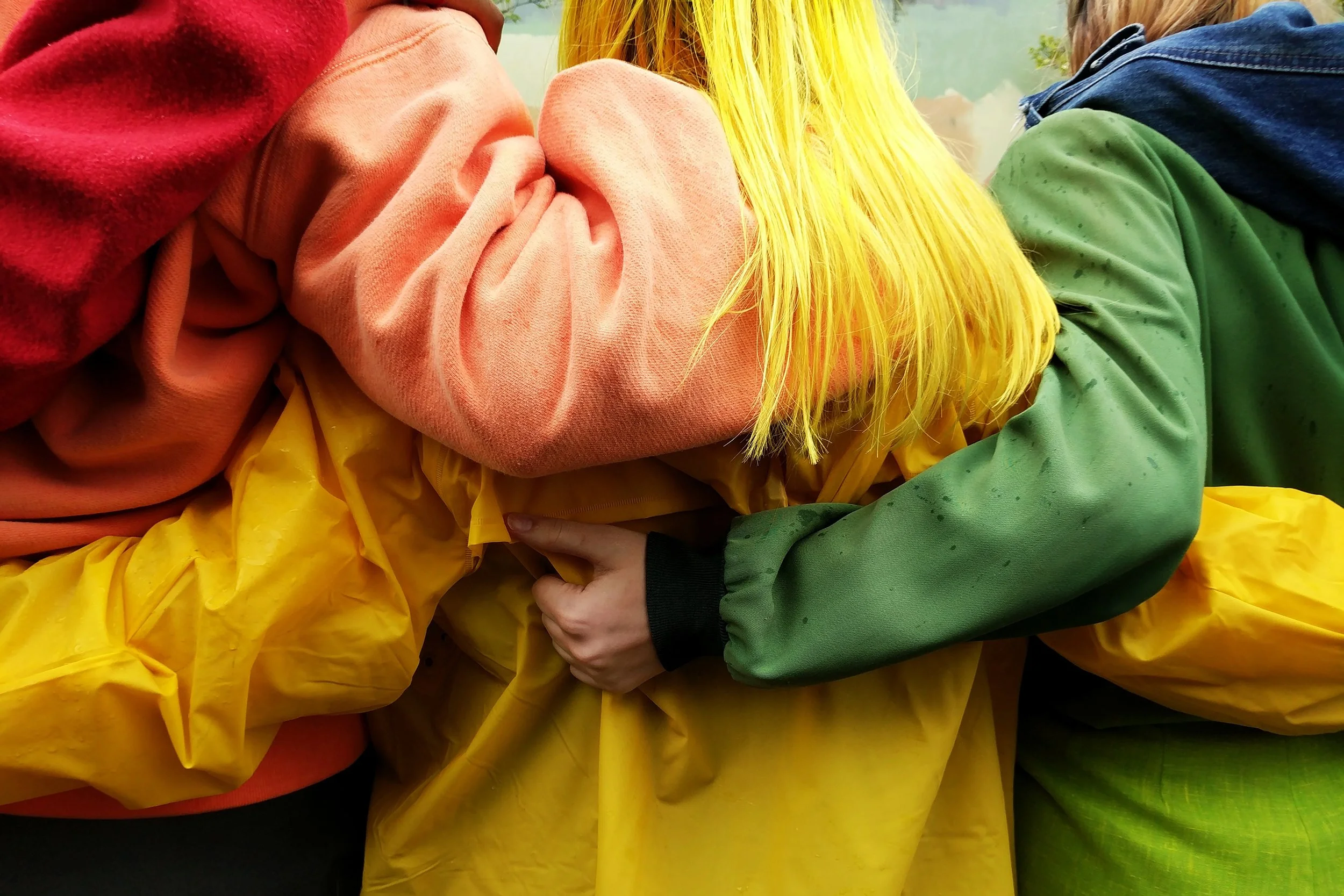 A group of people wearing colorful rain jackets hugging each other outdoors.