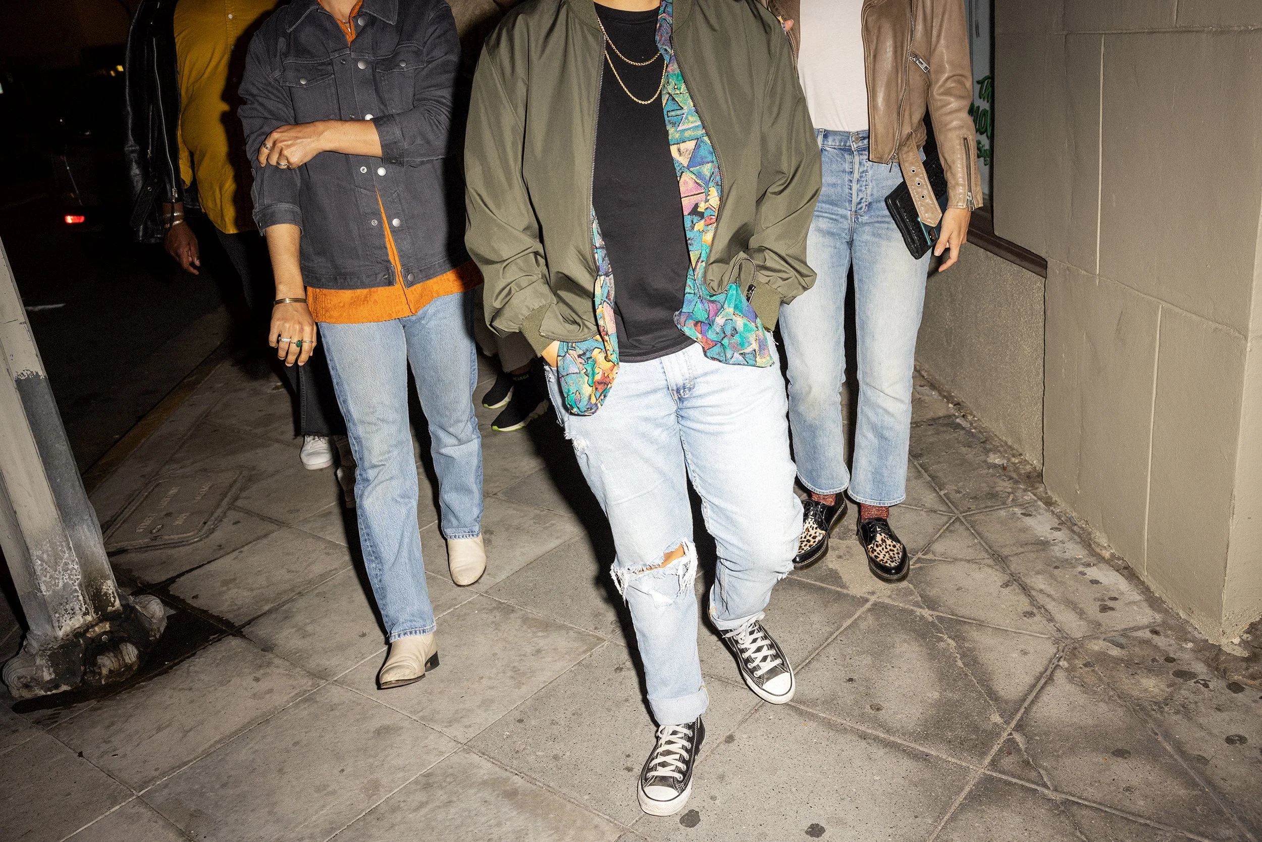 Group of women walking outside at night wearing casual clothing including jeans, jackets, and sneakers.
