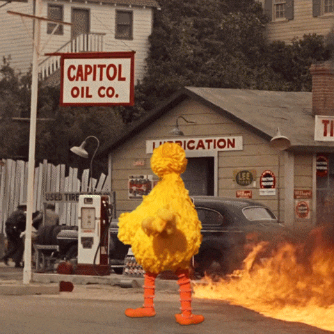 Sesame Street's Big Bird standing in front of a building as it explodes into fire.