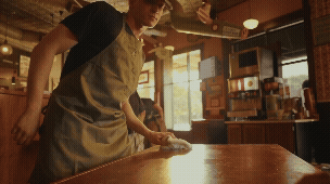 Person wiping a wooden table inside a café or restaurant