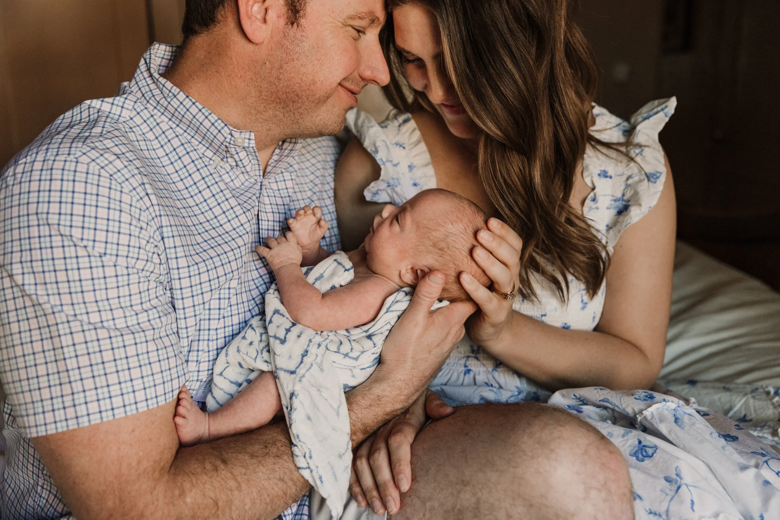 A man and woman are snuggled up closely looking down at their newborn baby with love and happiness.