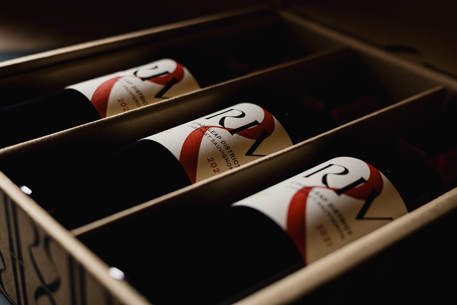 Three wine bottles in their branded box. The labels are creme, with black and red lettering. 