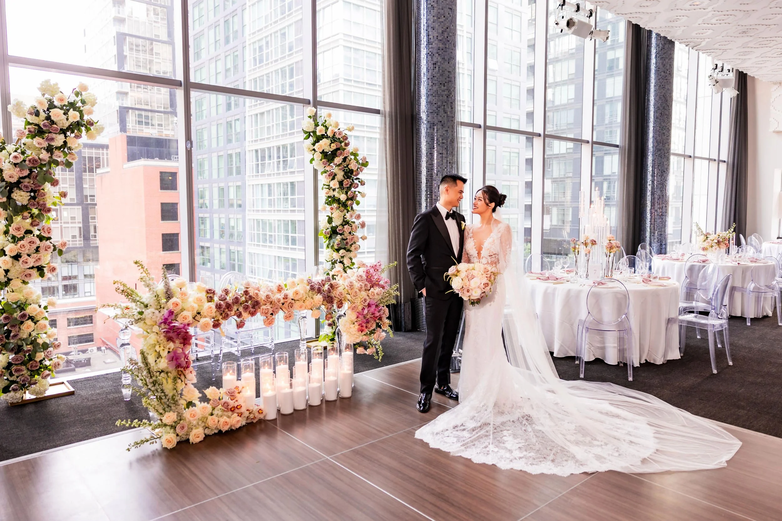 Bride and groom standing inside Malaparte in downtown Toronto with floral ceremony decor and city buildings visible through large windows