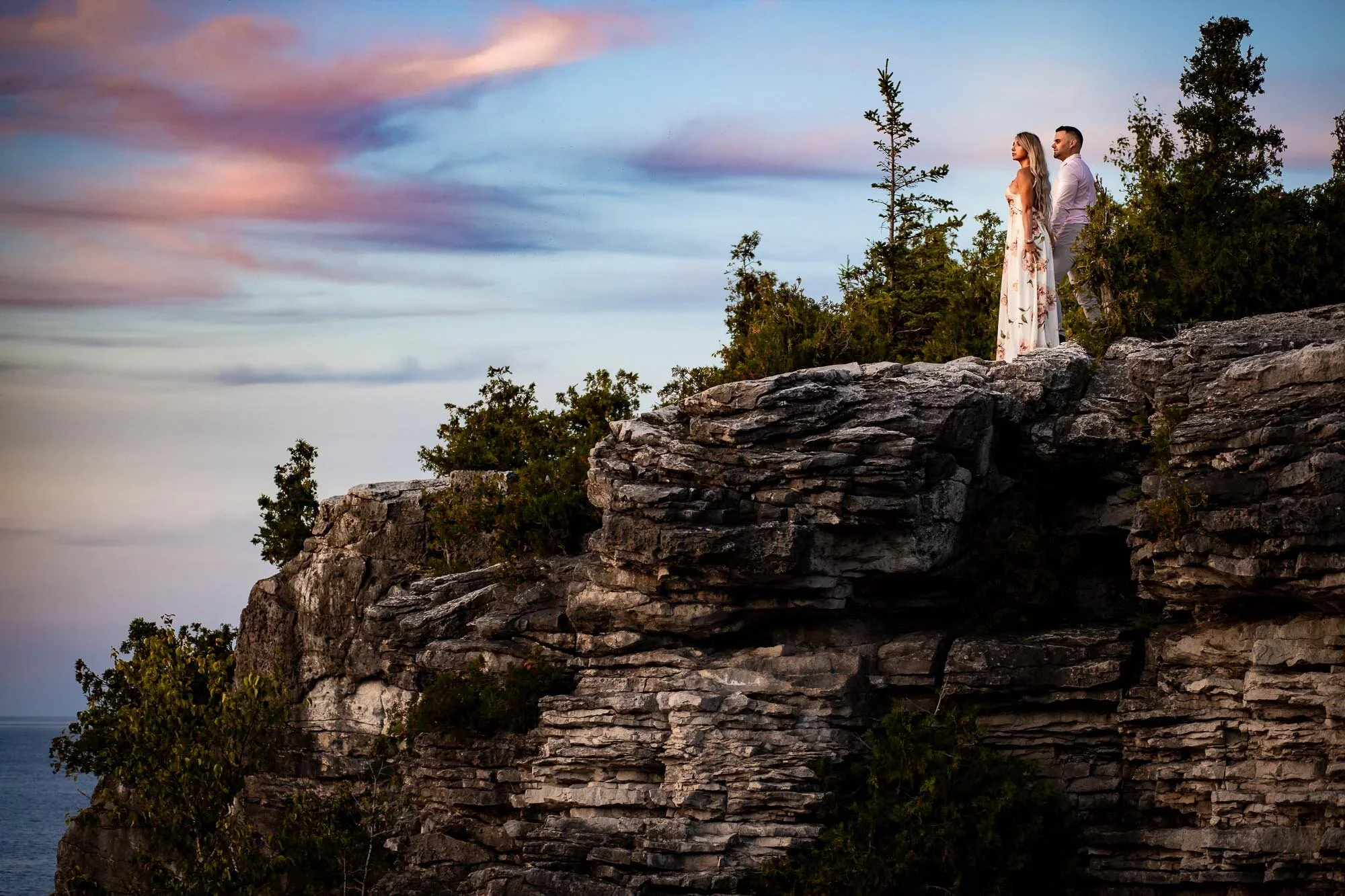 Tobermory engagement photo of a couple standing on dramatic limestone cliffs at sunset, overlooking Georgian Bay near the Grotto in Bruce Peninsula National Park.