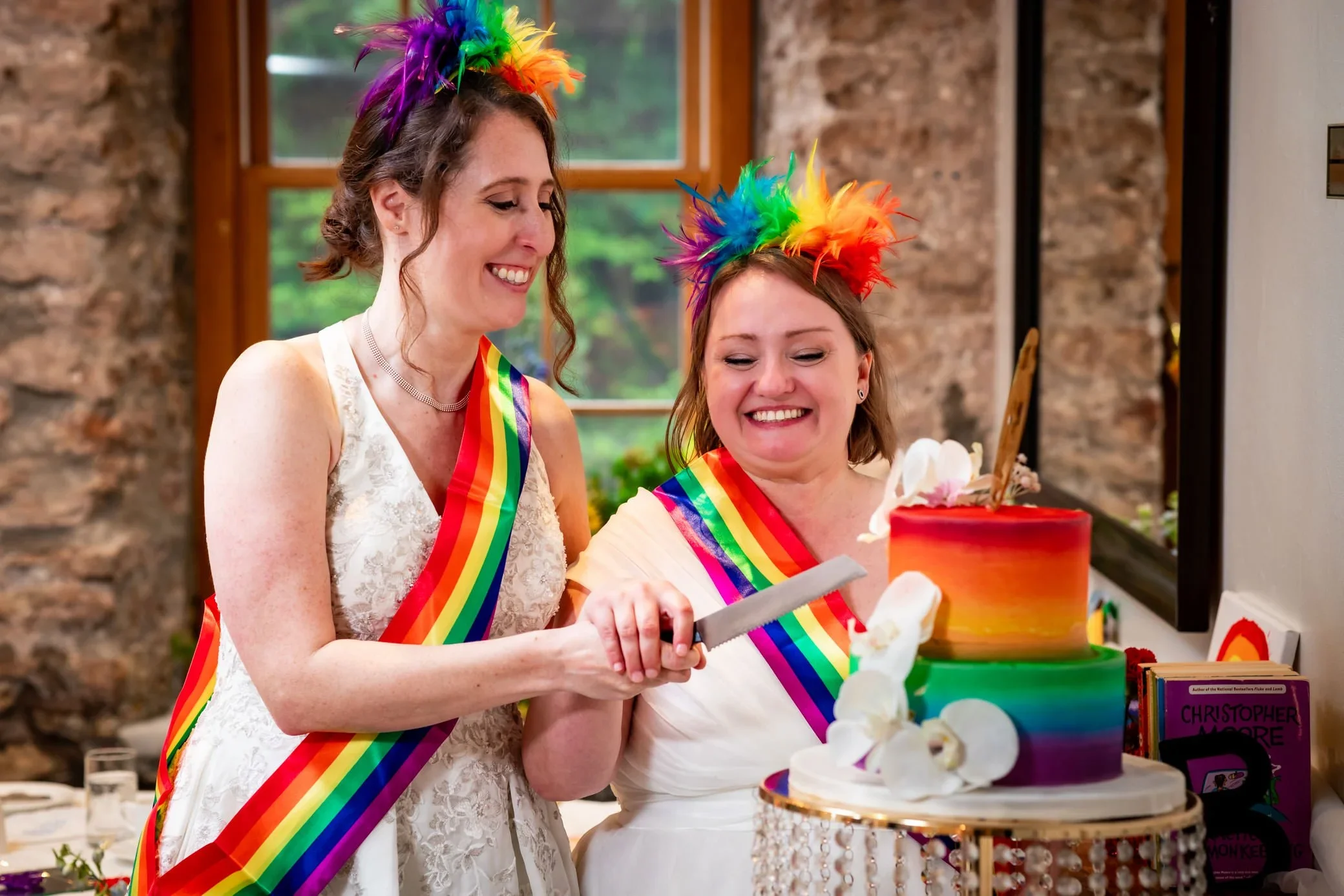 Queer couple cutting rainbow wedding cake at Millcroft Inn in Elora Ontario, joyful LGBTQ wedding celebration