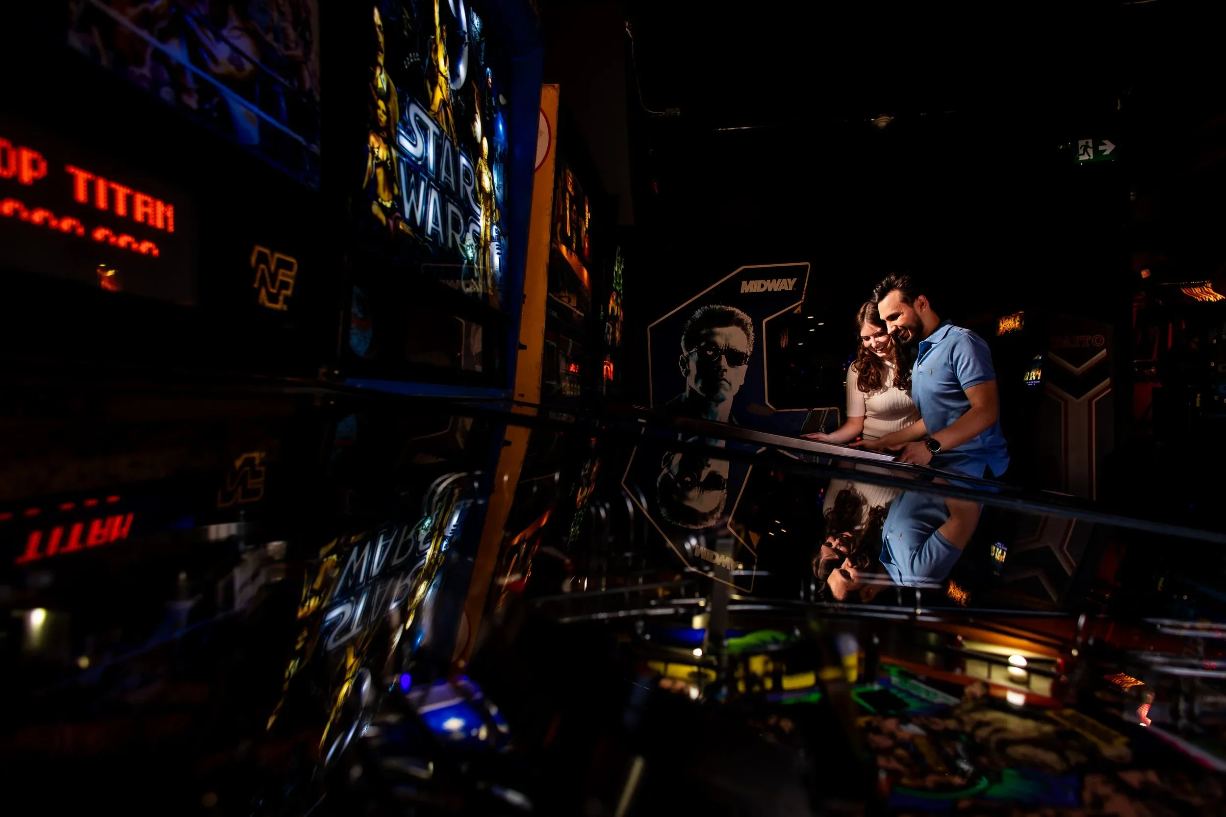 Couple playing pinball during their engagement session at Tilt Arcade in Toronto, reflected in the glass of an arcade machine.