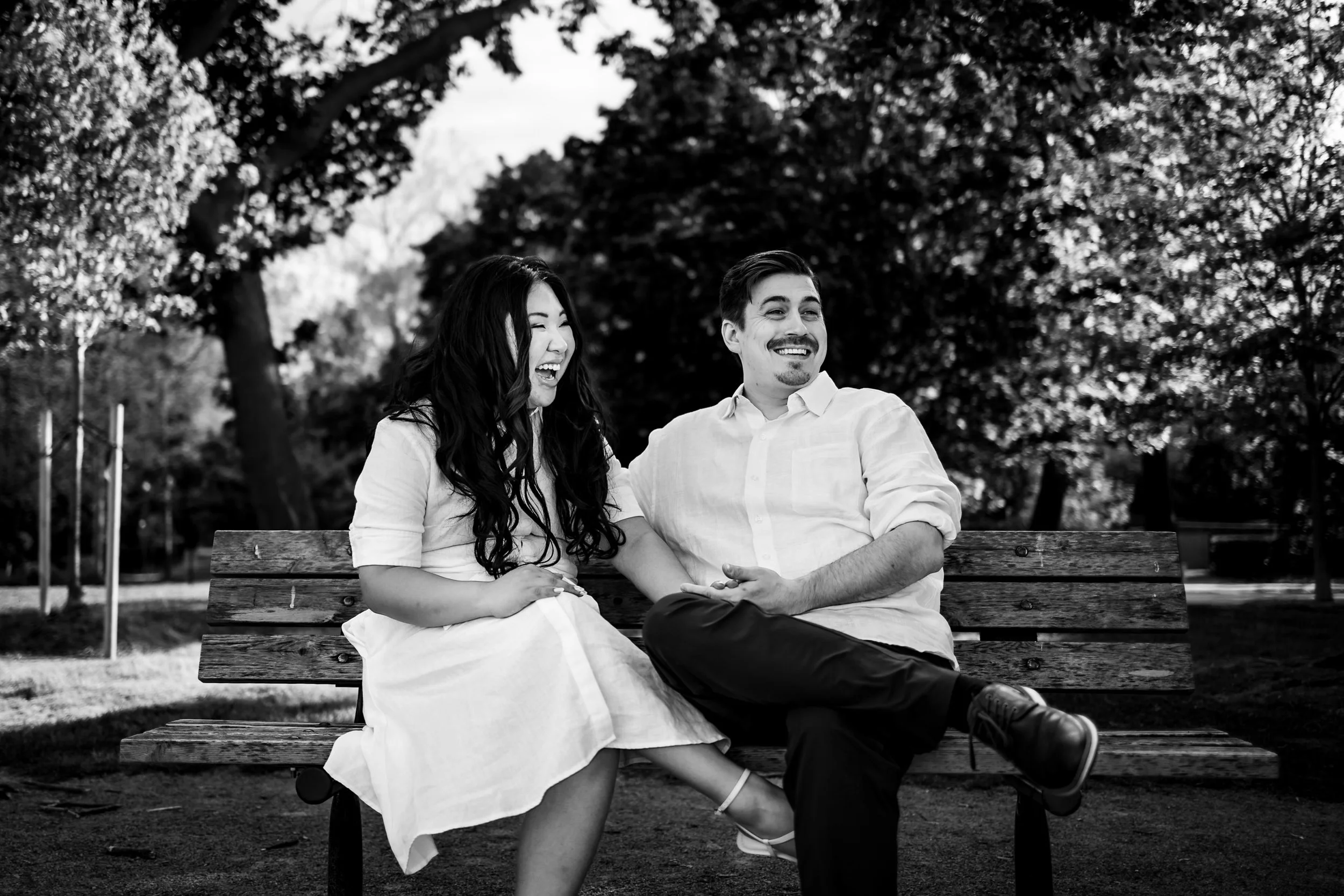 Black and white engagement photo couple laughing bench Niagara on the Lake