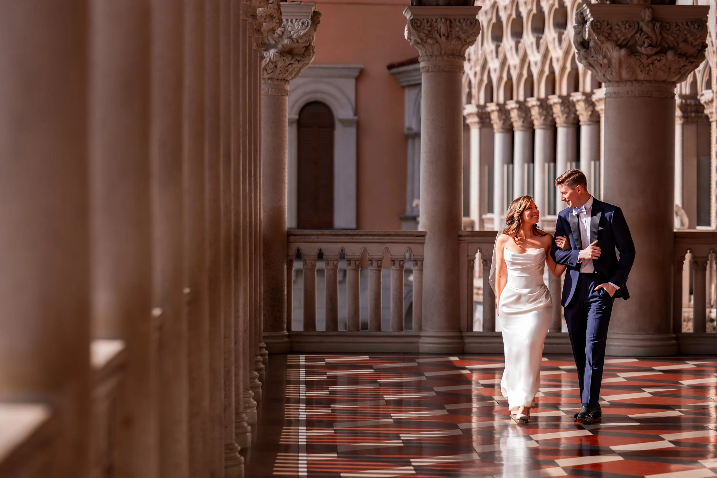 Bride and groom walking together through the grand architecture of The Venetian in Las Vegas during an elegant destination wedding portrait session.