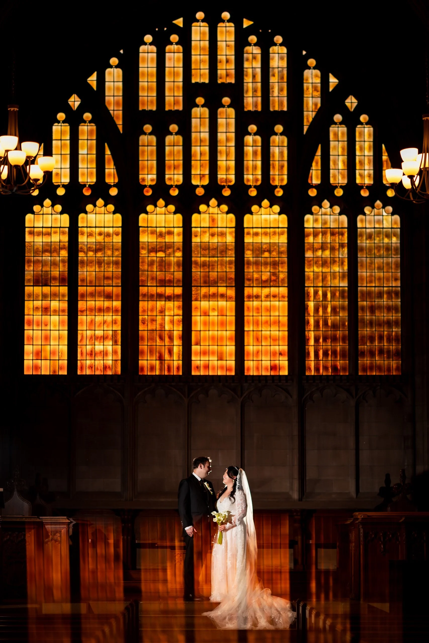Indoor couple portrait at Knox College Chapel in Toronto, bride and groom standing in warm golden window light beneath towering stained glass during their wedding day