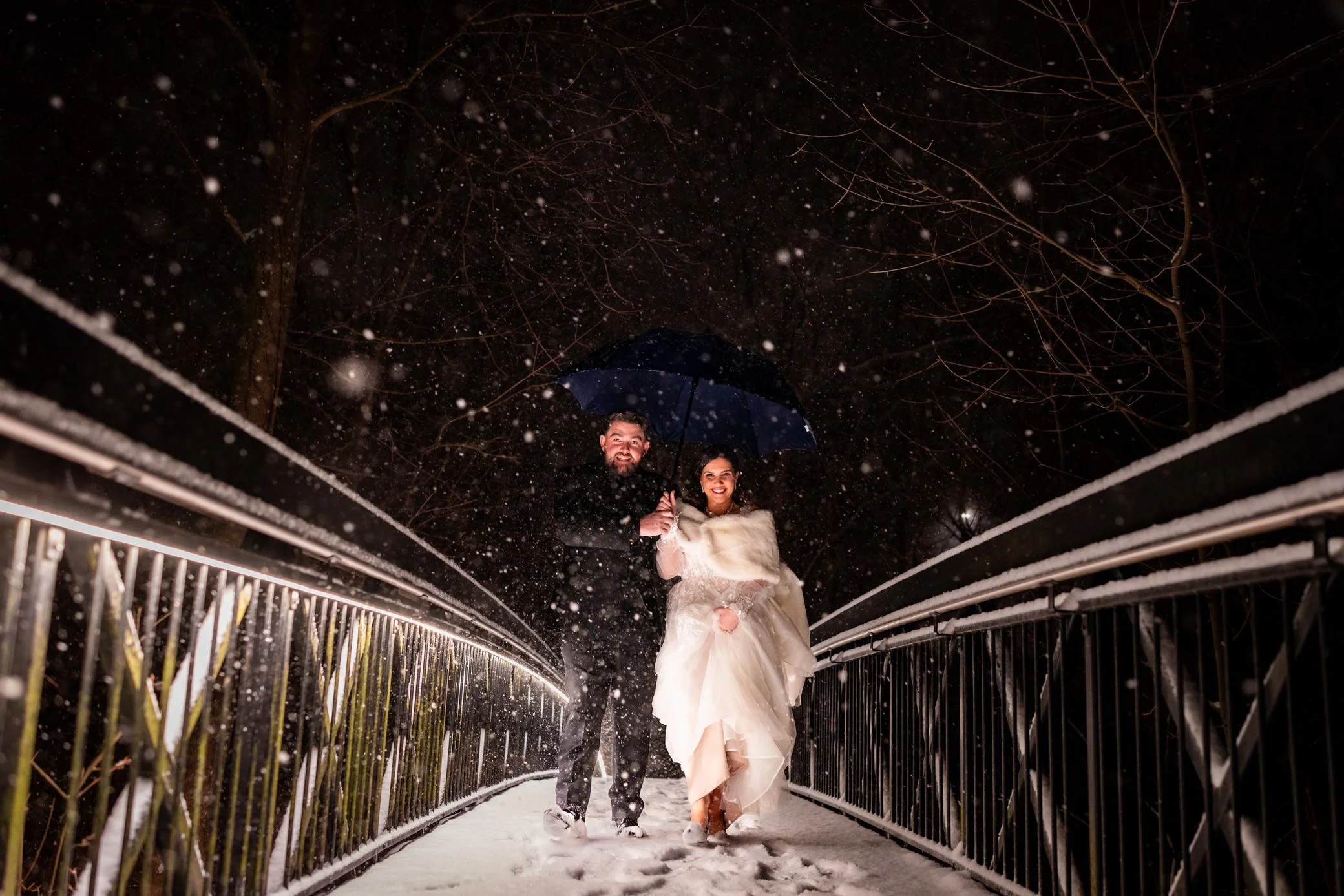 Bride and groom walking on a snowy bridge at Ancaster Mill during a winter wedding