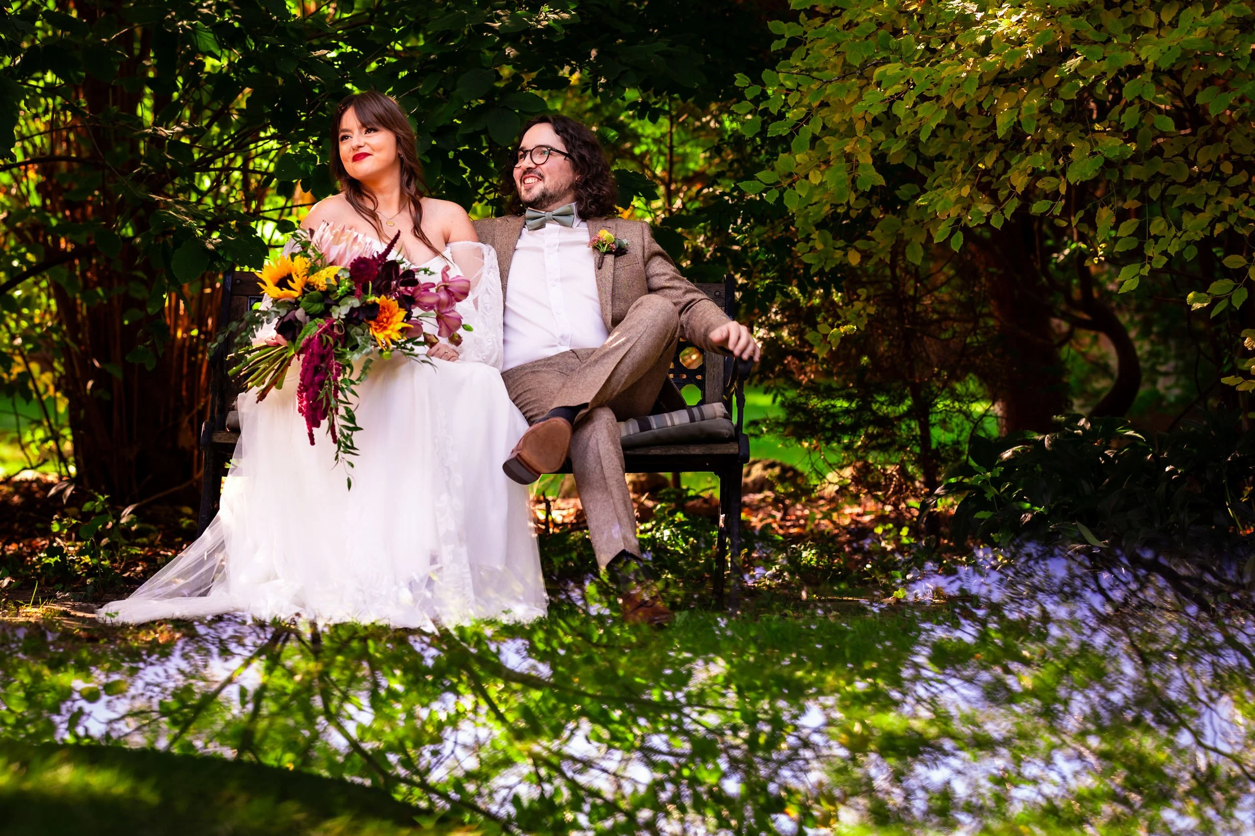 Bride and groom sitting together on a bench during a romantic garden wedding portrait surrounded by greenery