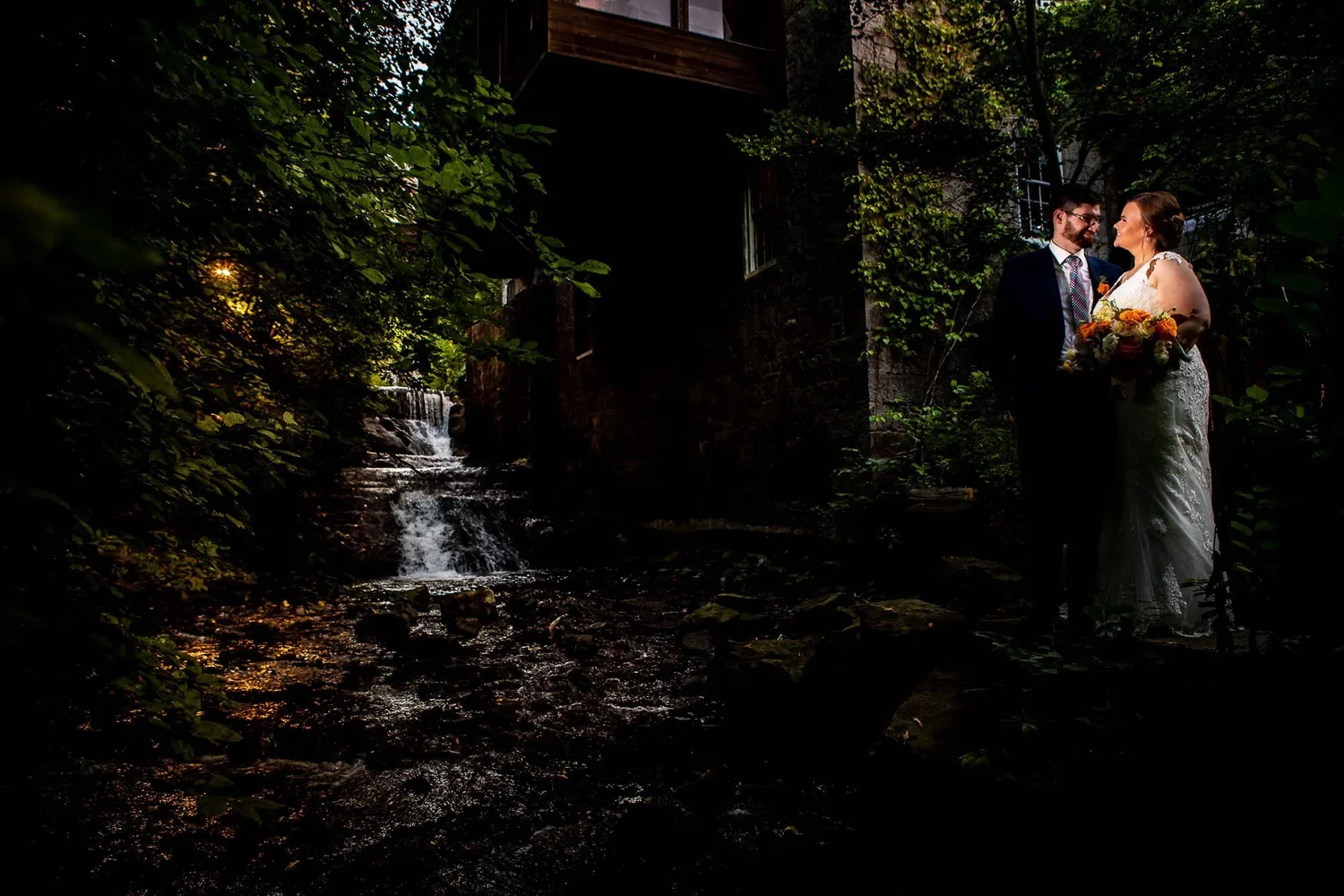 Creative nighttime wedding portrait of a couple beside the waterfall at Ancaster Mill in Ontario.