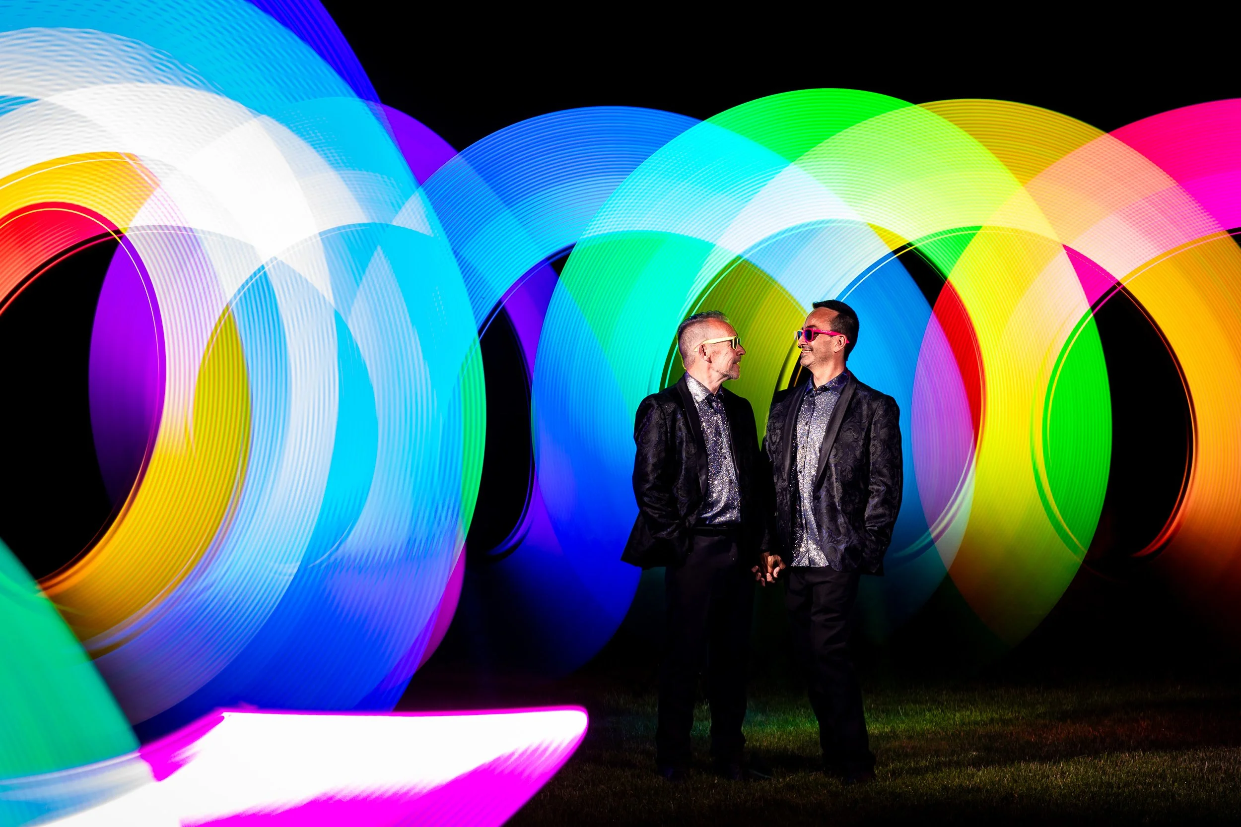 Same sex couple holding hands in a creative nighttime portrait with colourful light painting, photographed by a Toronto LGBTQ wedding photographer