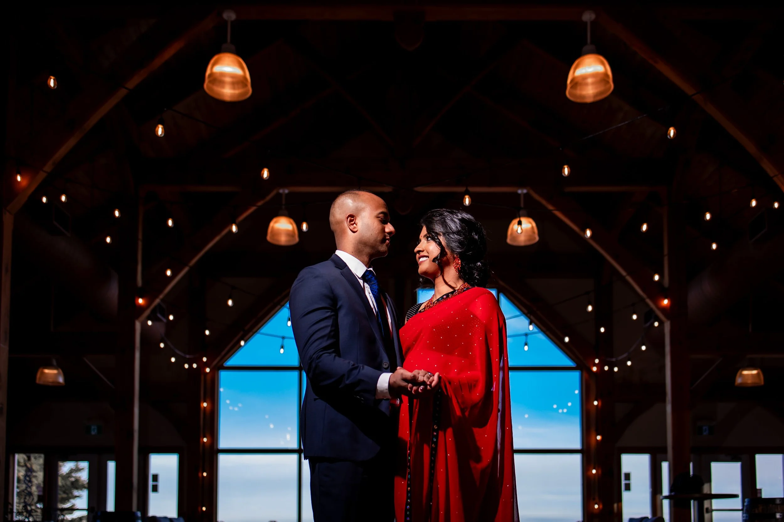 Couple kissing during their wedding ceremony at Trail Hub with warm string lights and wood interior