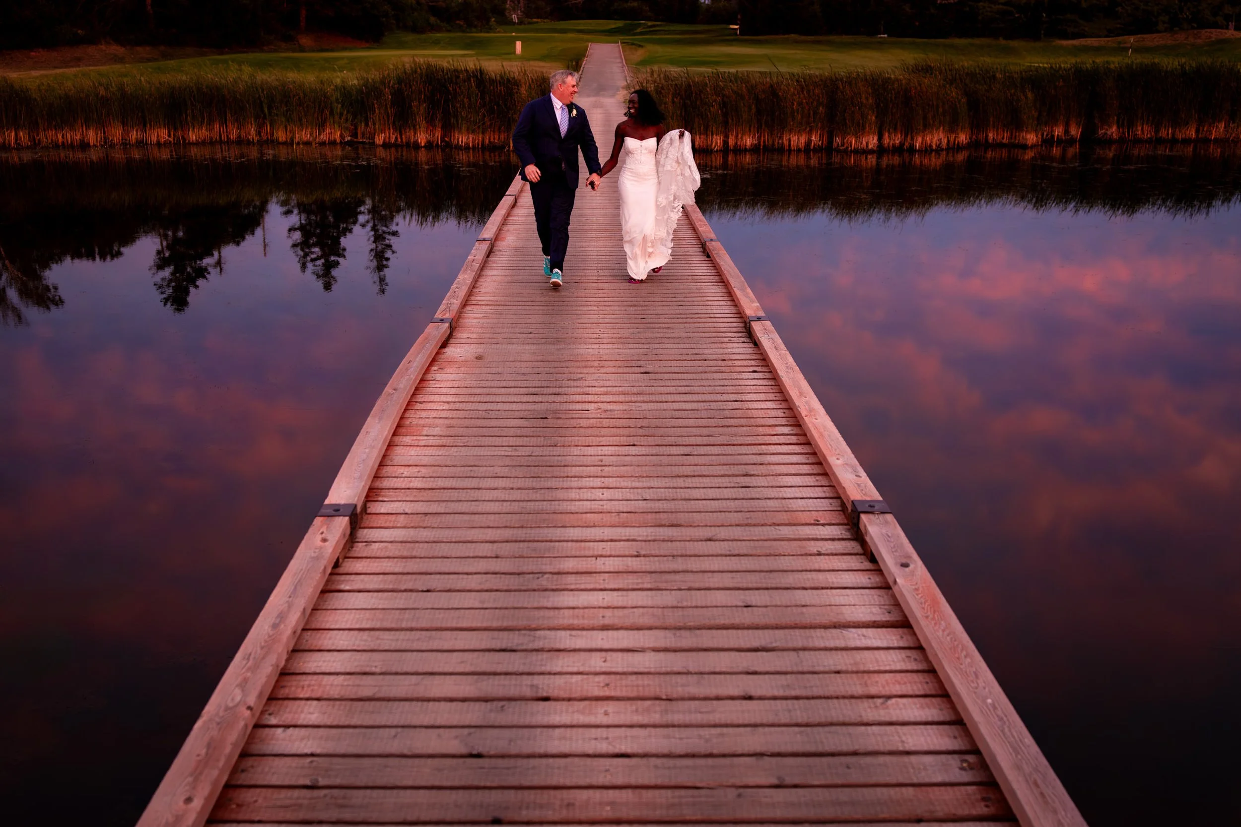 Bride and groom walking hand in hand on a dock during a romantic waterfront wedding portrait at sunset