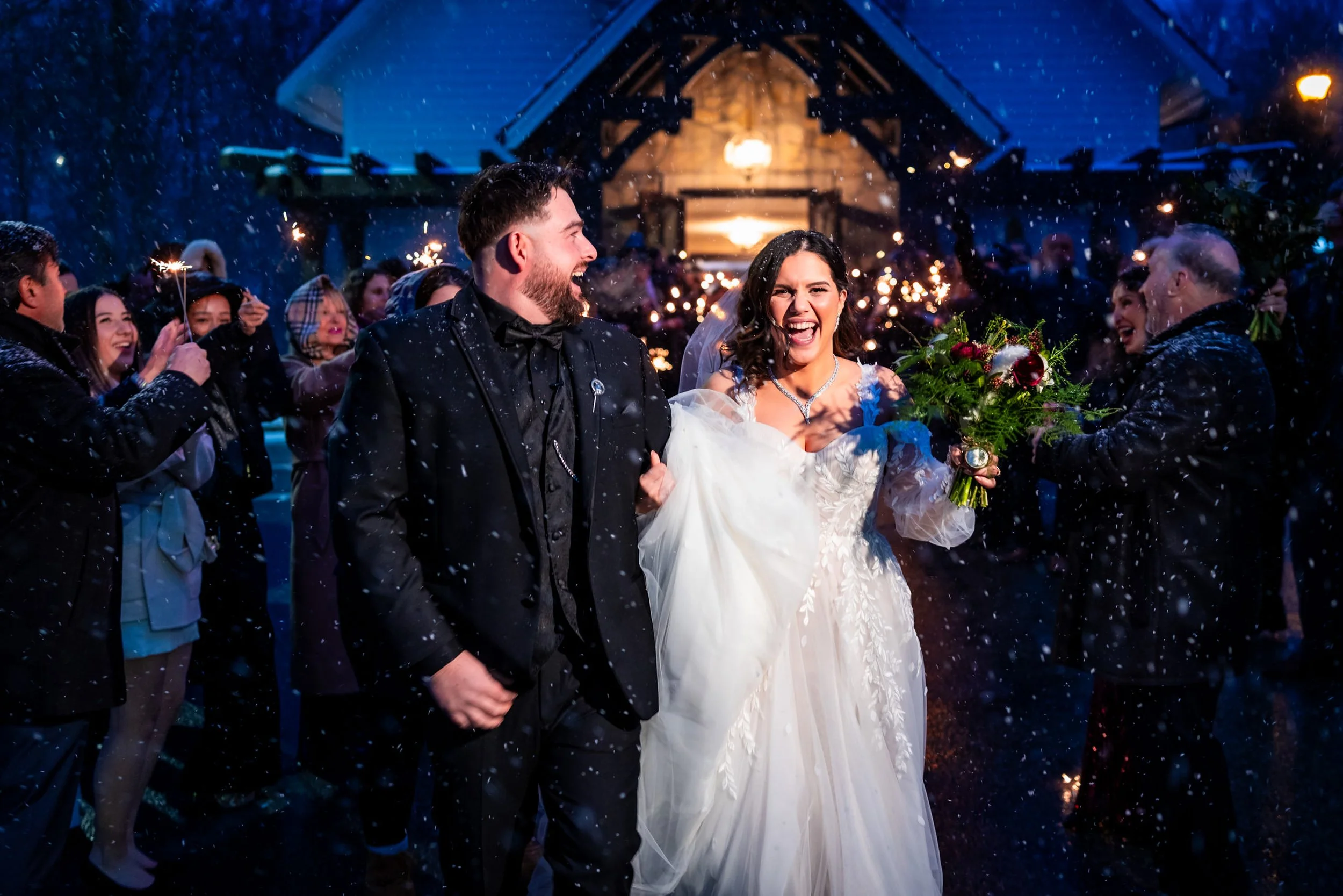 Bride and groom running through a snowy sparkler exit at night surrounded by cheering guests