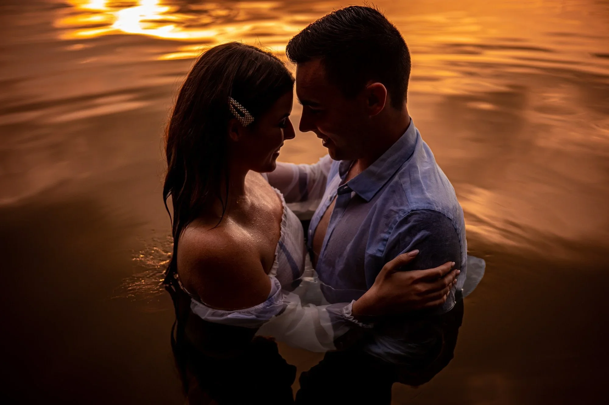 Creative engagement photo of a couple standing in the water at sunset, used for engagement photo tips for couples planning natural, romantic, and meaningful engagement photos.
