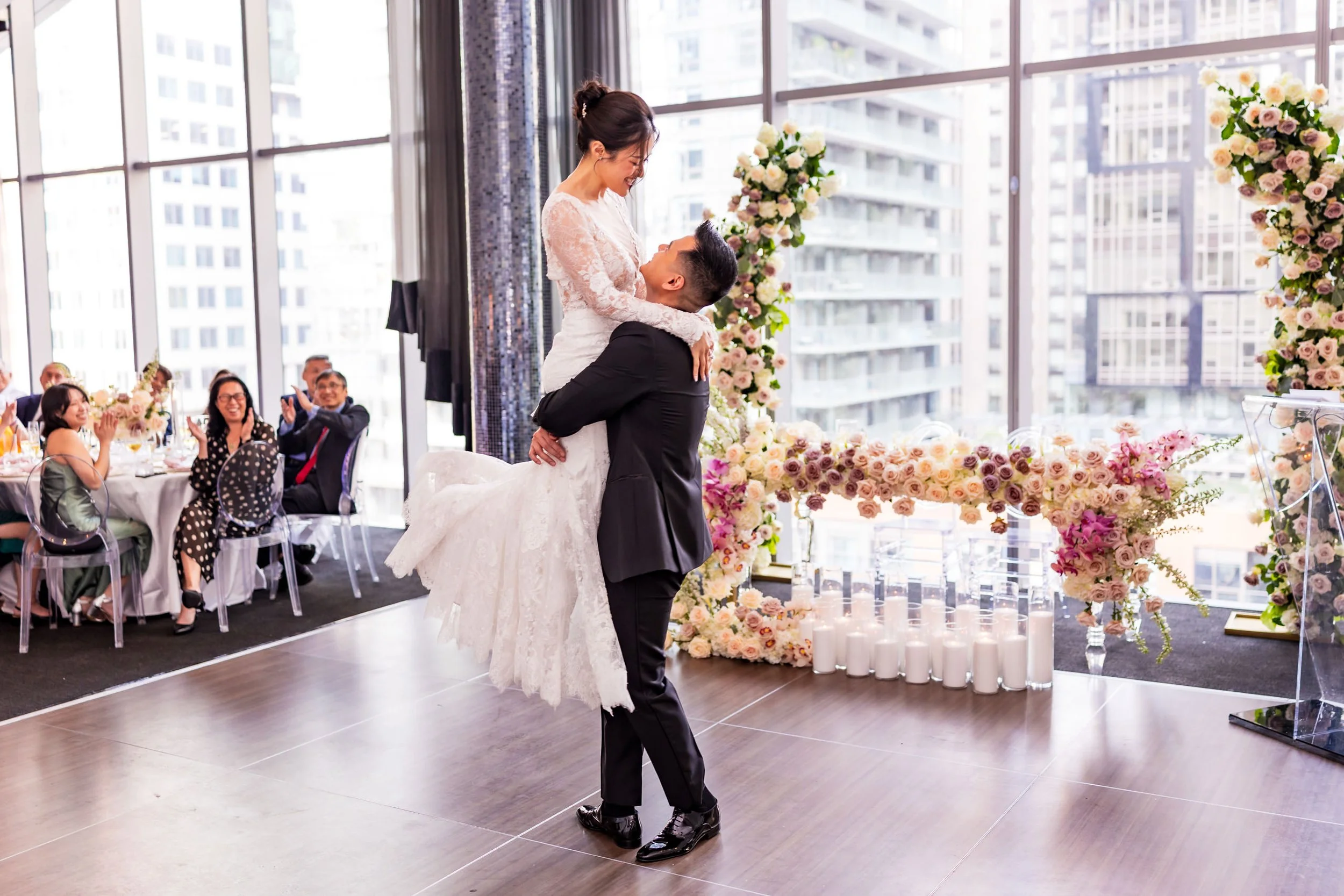 Terri and Jeremy share a joyful first dance at Malaparte in downtown Toronto, surrounded by blush and cream floral decor and floor candles with the city skyline in the background