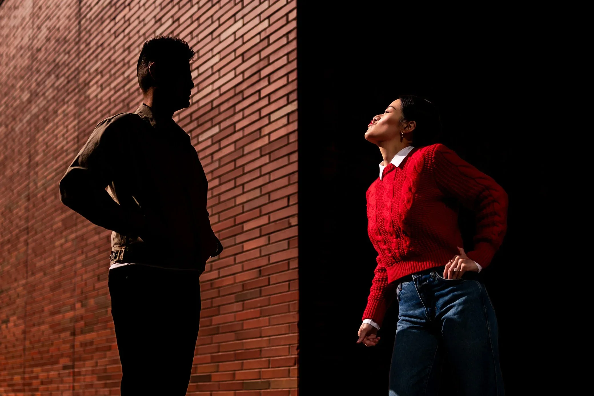 Toronto Distillery District engagement photos of a couple in dramatic light against a brick wall during a creative urban engagement session in Toronto.
