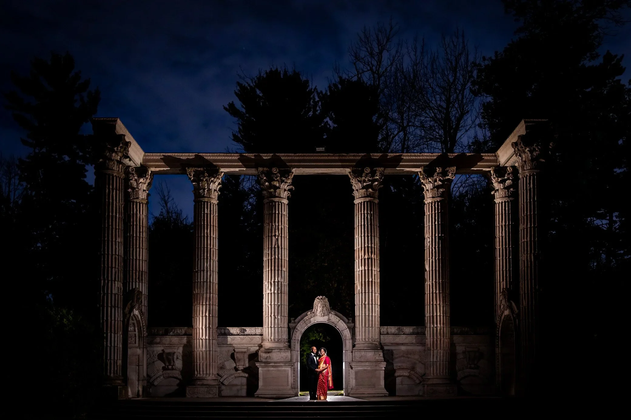 Couple standing under the Guild Inn Estate columns at night in Scarborough Toronto, dramatic nighttime wedding portrait at the famous Guild arches.