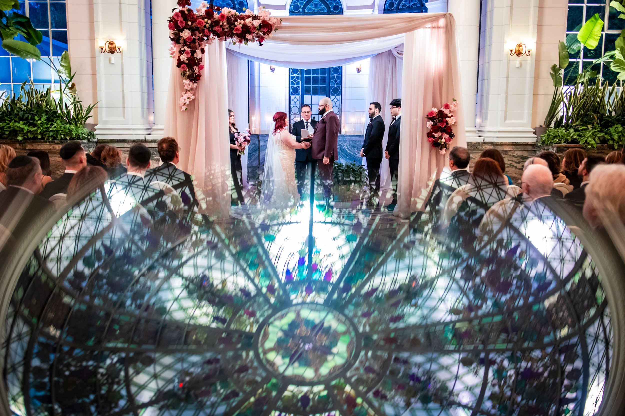 Jewish wedding ceremony at Casa Loma Toronto under a chuppah with dramatic stained glass reflection, elegant and candid wedding photography moment